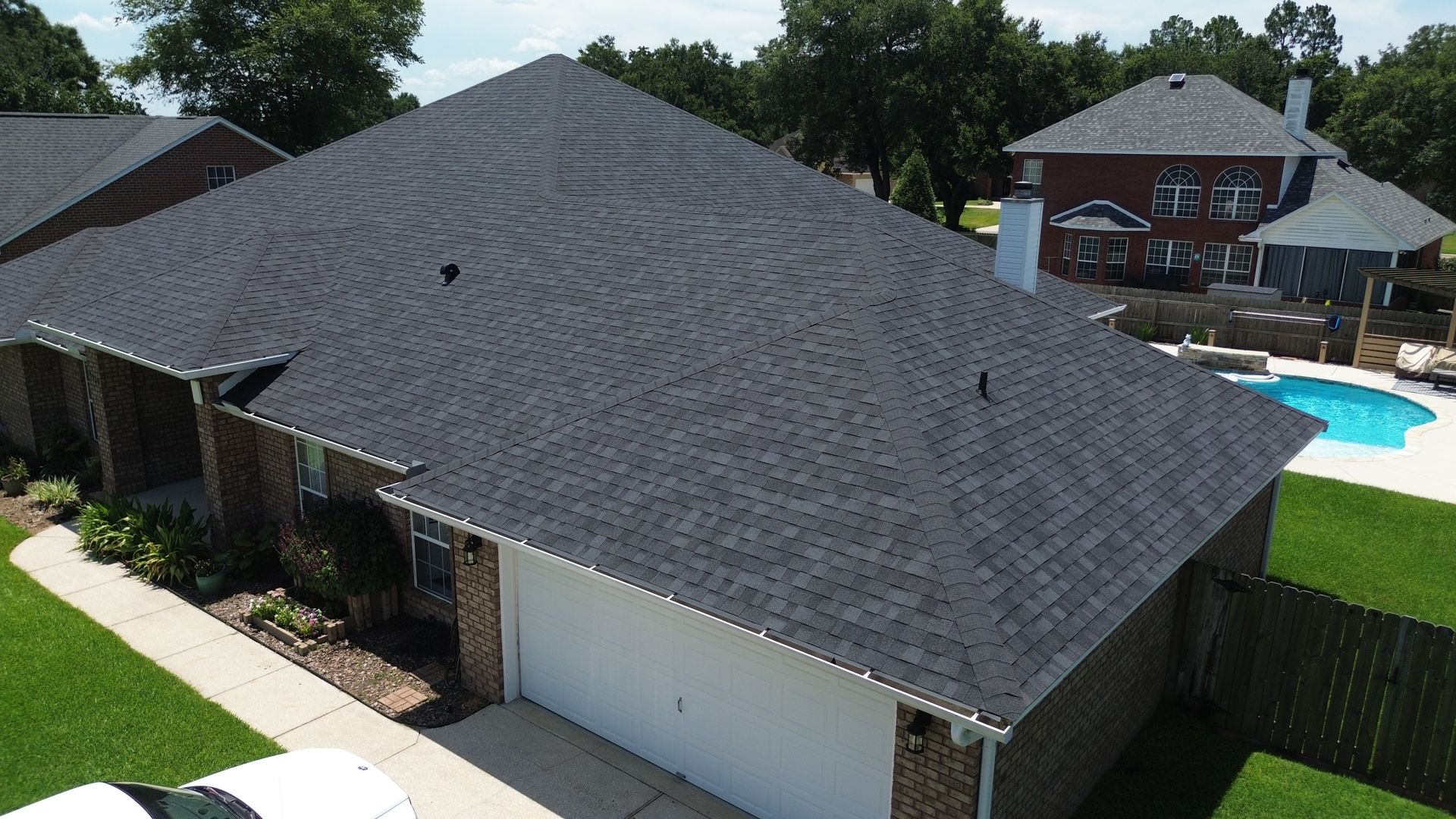 Aerial view of a house with a dark roof, garage, and backyard pool near a wooden fence.