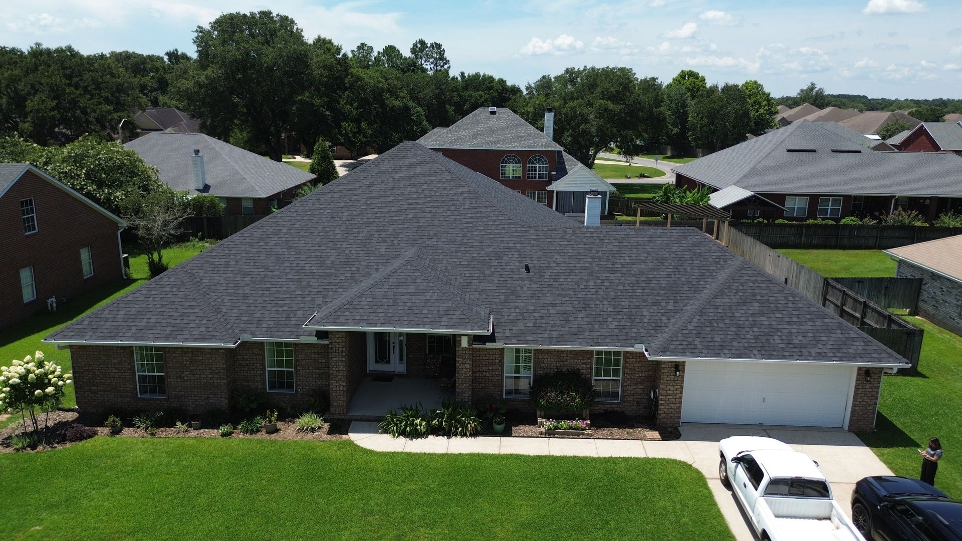 Aerial view of a brick suburban house with a gray roof, white garage, and white car in the driveway.