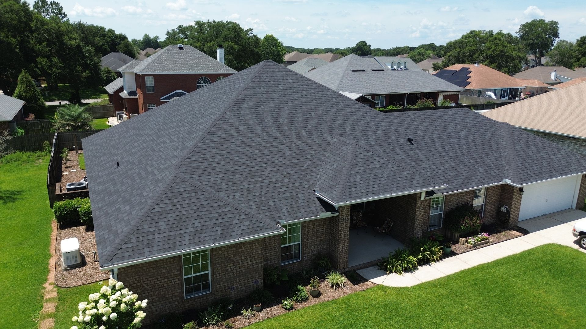 Aerial view of a single-story house with a dark gray roof and brick exterior in a suburban neighborhood
