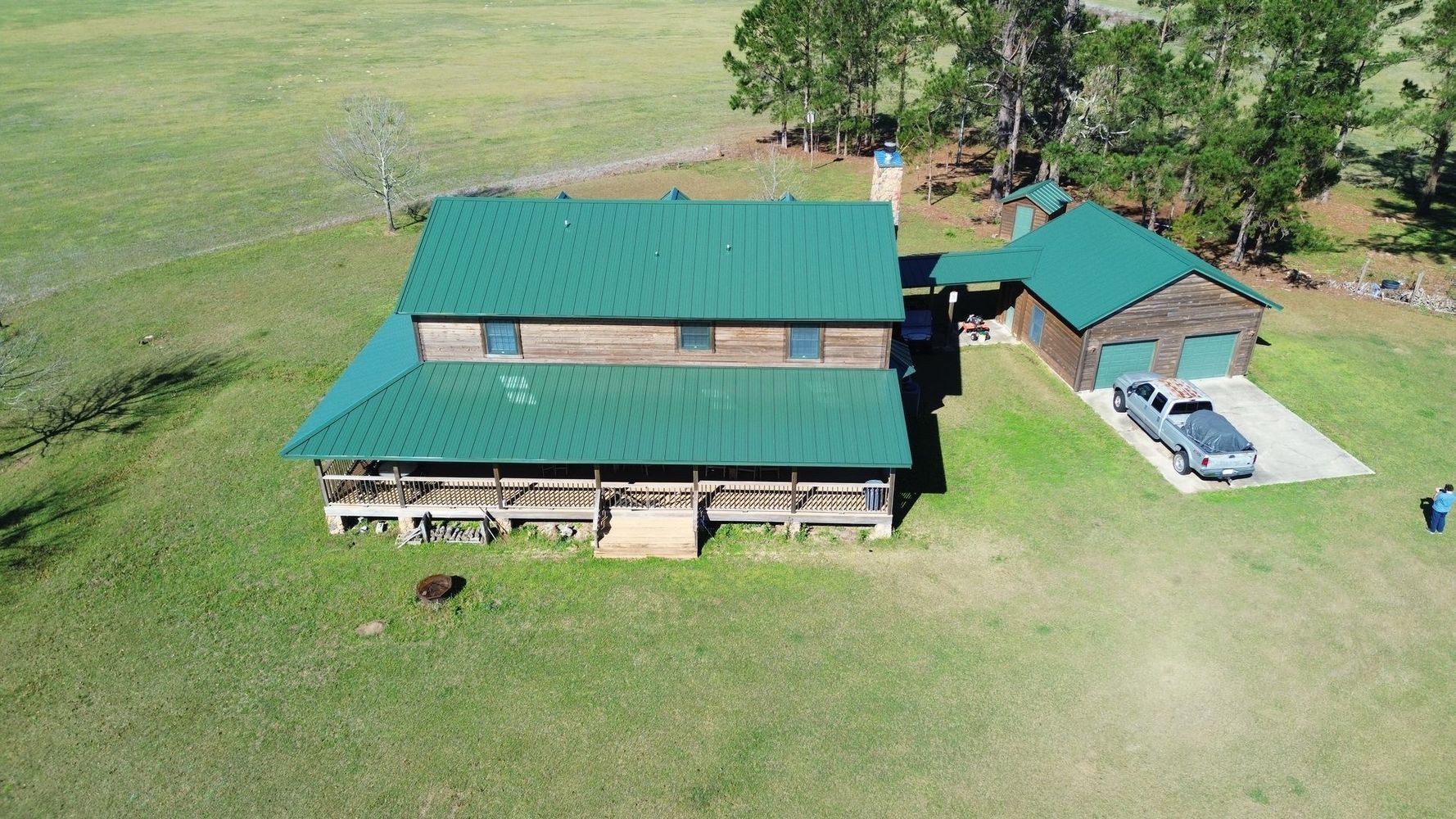 Aerial view of a green-roofed house with a carport and parked truck on a grassy rural property