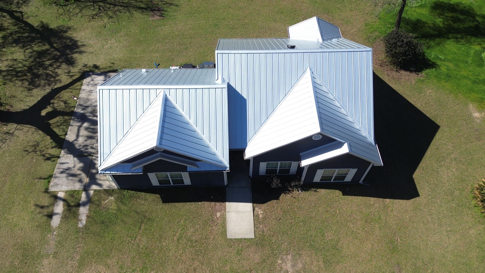 Aerial view of a white-roofed house with two front gables and a concrete walkway in a grassy yard.