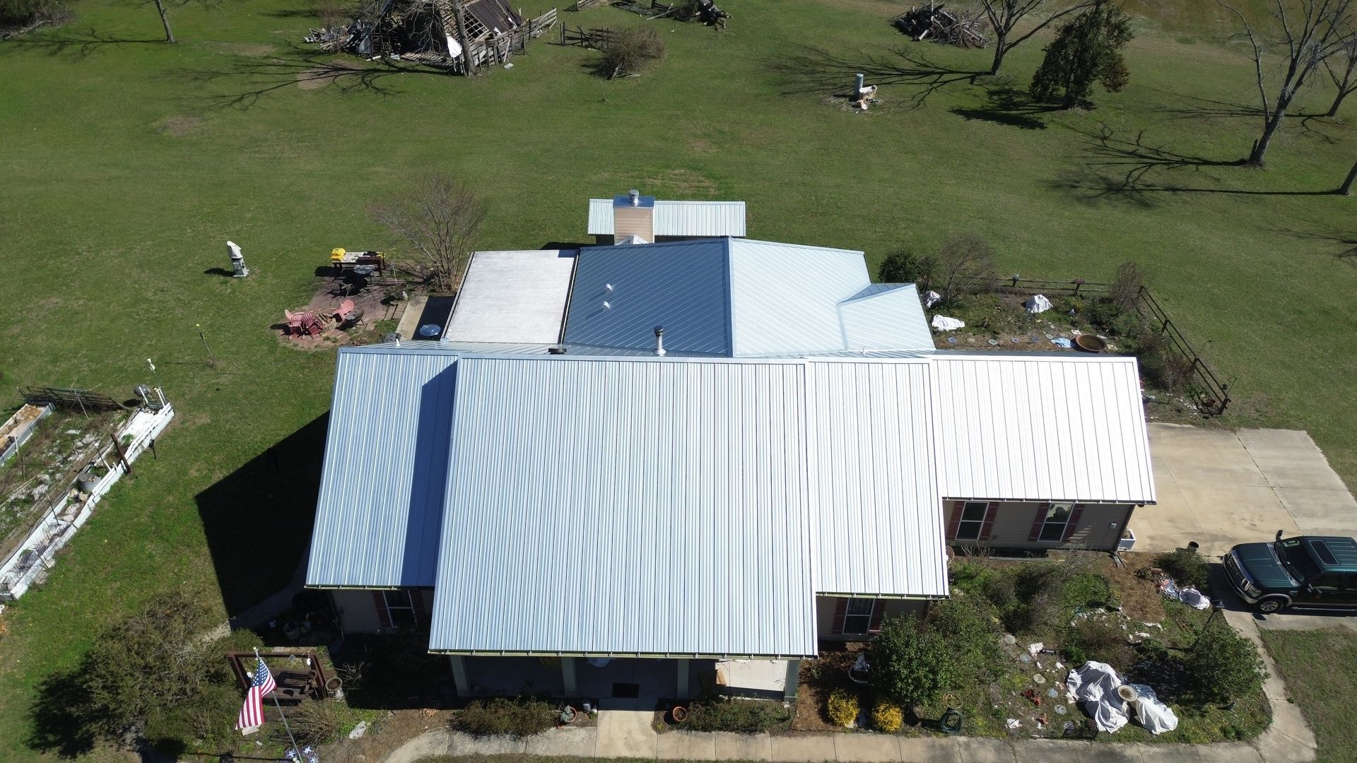 Aerial view of a white-roofed house surrounded by green grass and scattered trees