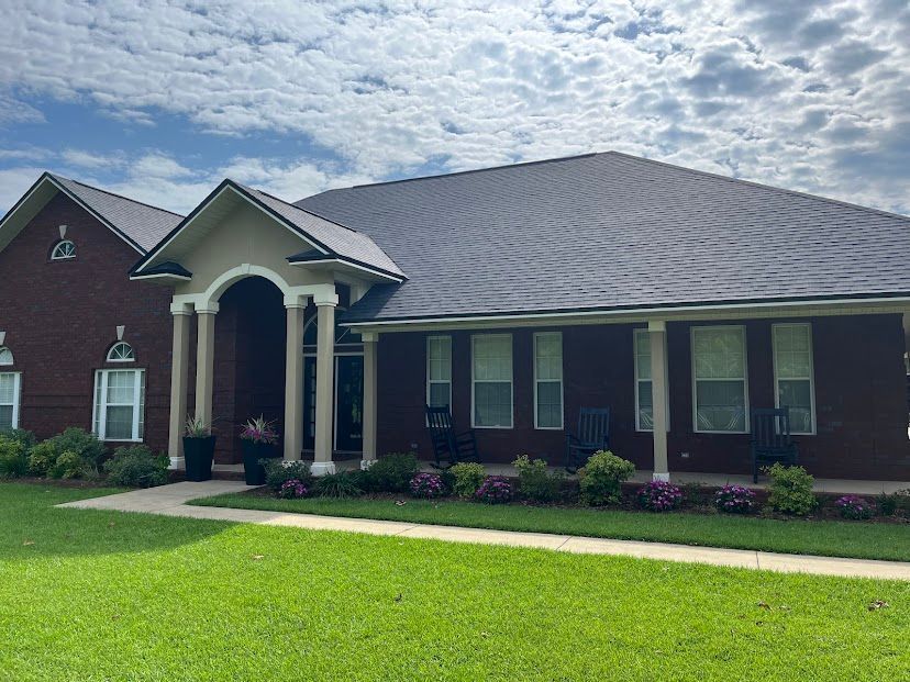 Single-story brick house with arched front porch, gray roof, and green lawn under a cloudy sky