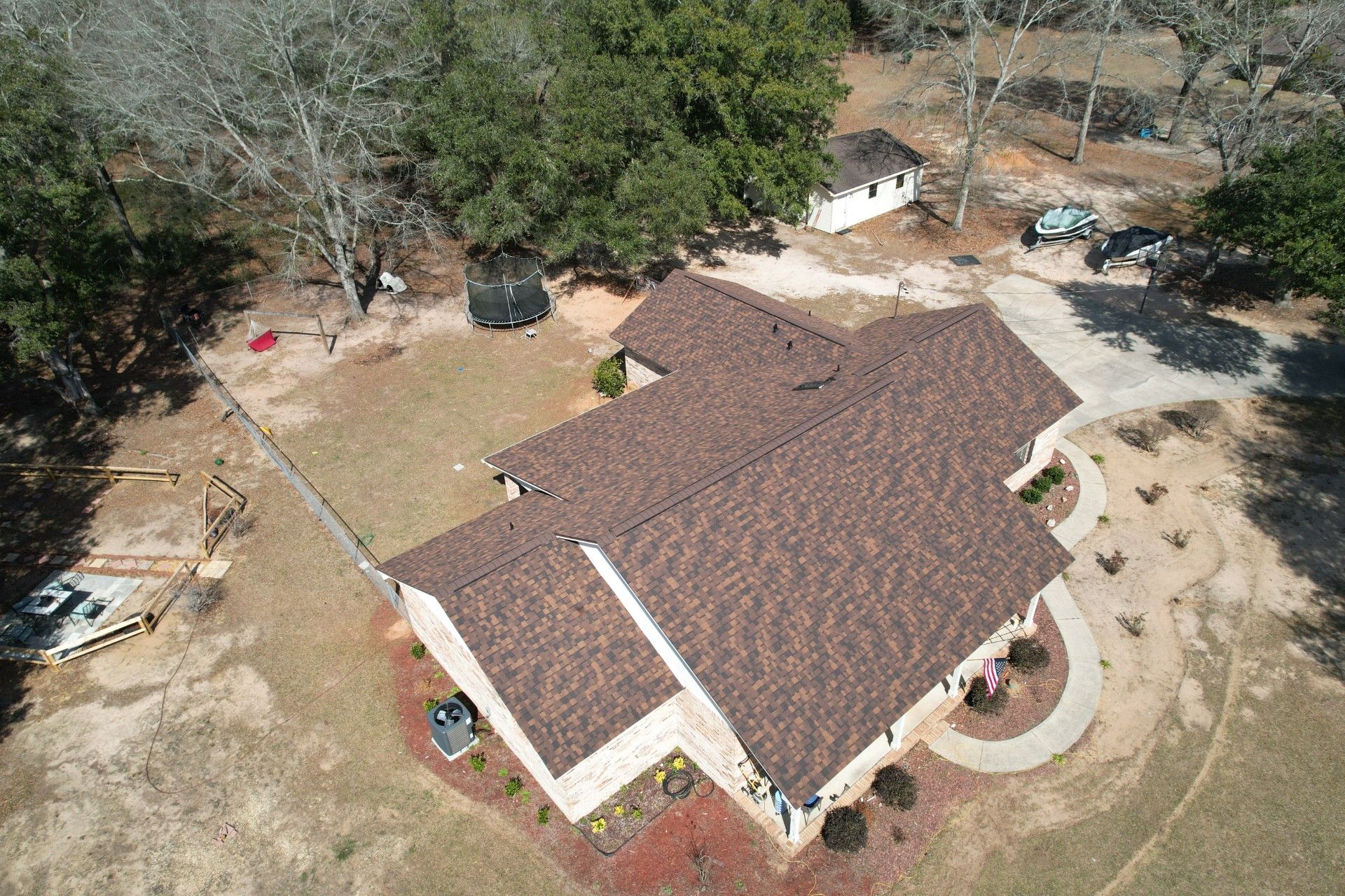 Aerial view of a house with a brown roof surrounded by trees and a yard