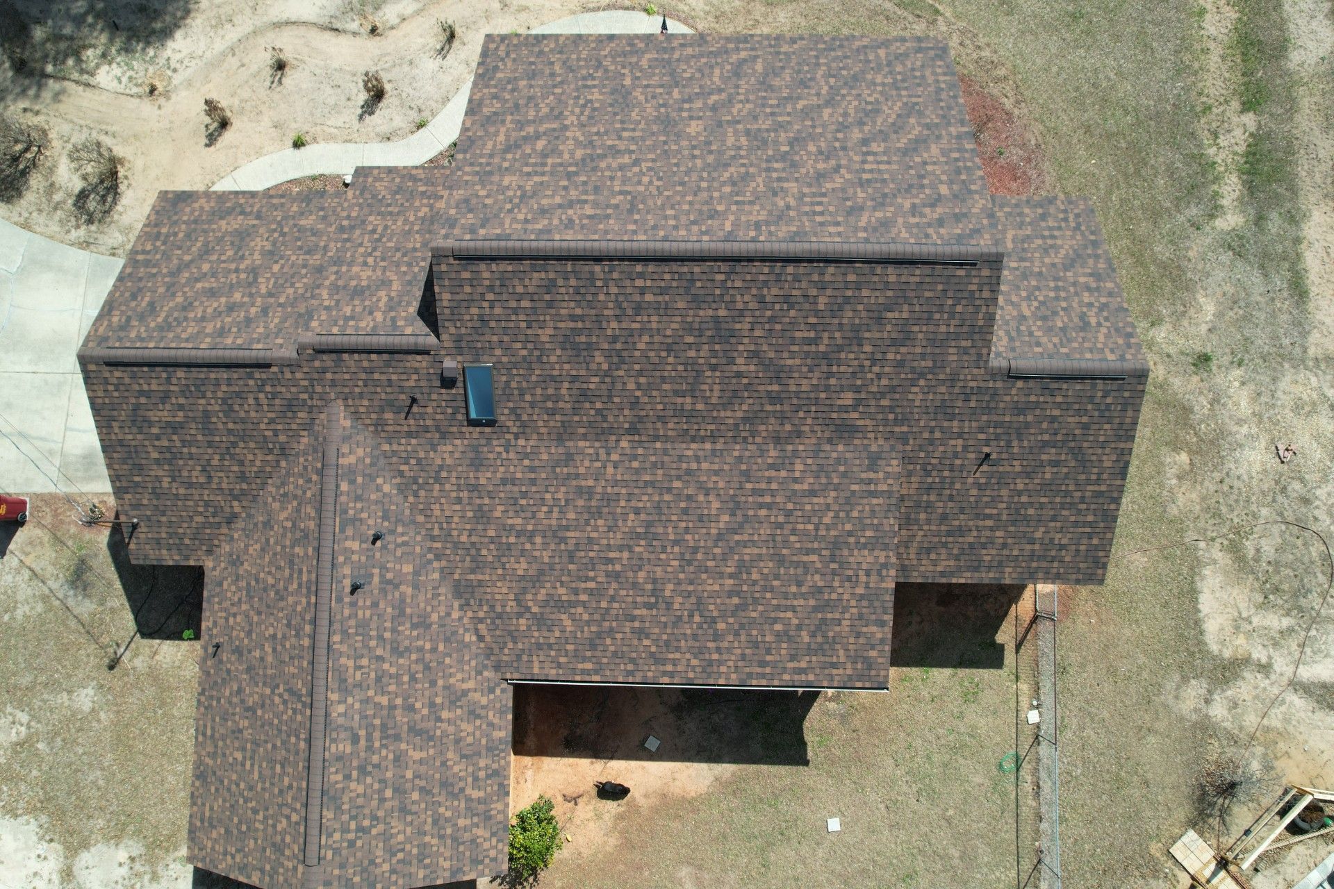 Aerial view of a brown-shingled house roof with multiple sections and surrounding yard