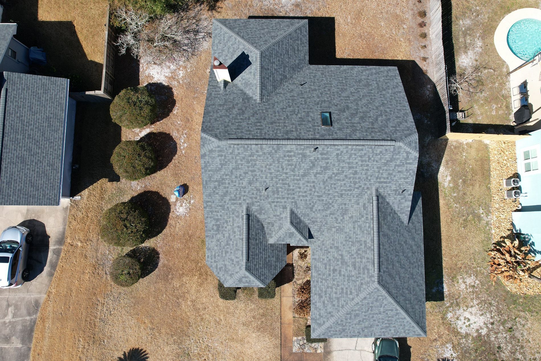 Aerial view of a gray-roofed house with a small yard and nearby parked vehicles