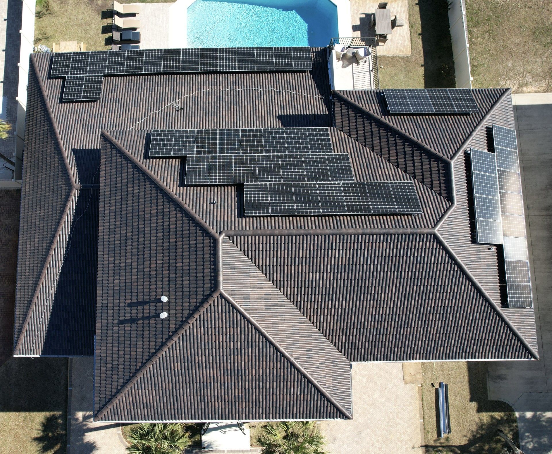 Aerial view of a house with dark shingle roof and a backyard pool.