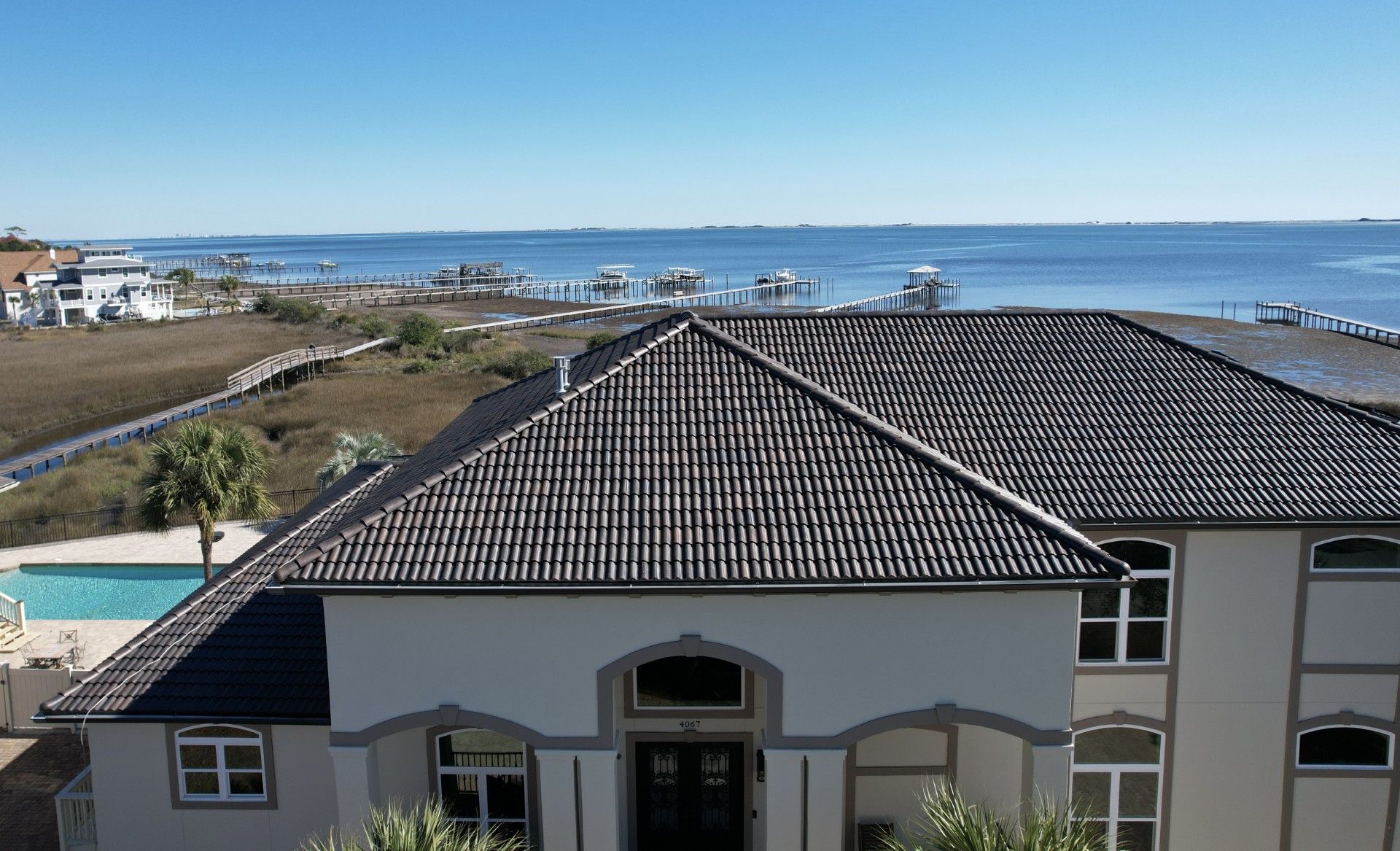 Coastal house with dark tiled roof overlooking a marina and blue ocean under a clear sky