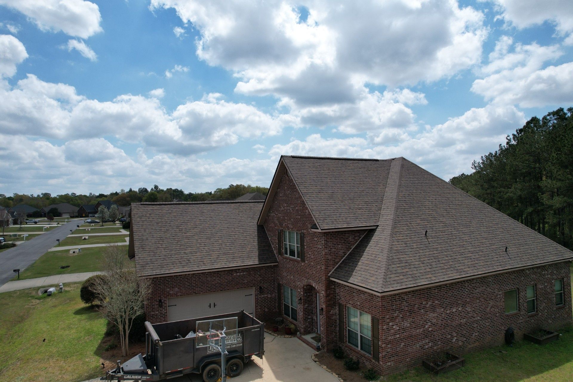 Brick house with a shingled roof and driveway under a partly cloudy sky.