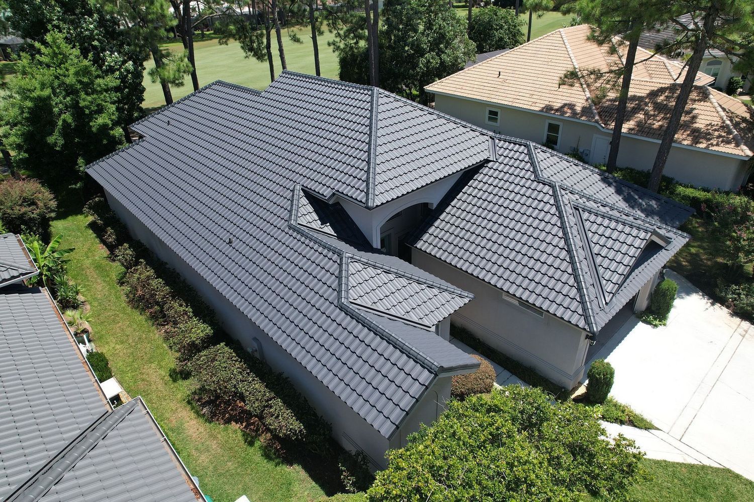 Aerial view of a dark gray tiled roof with multiple gables and trees surrounding the house