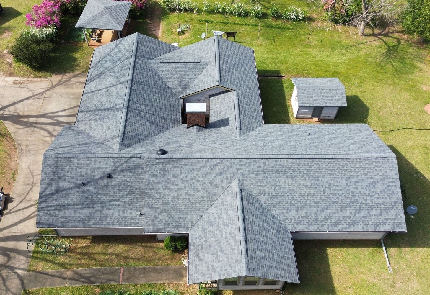 Aerial view of a gray-shingled house with a lawn, driveway, and small detached shed.