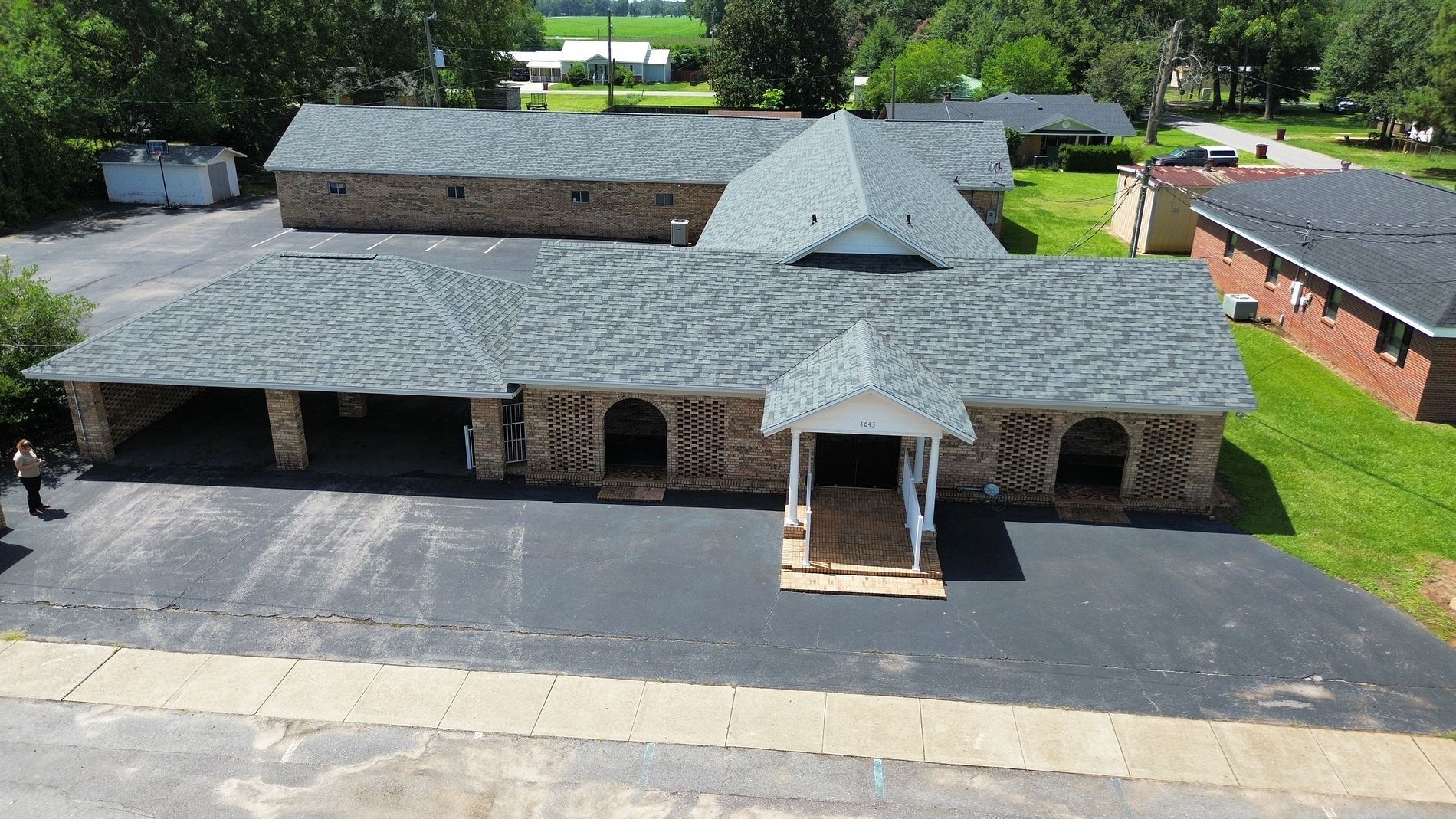 Aerial view of a gray-roofed building with a central entrance and surrounding greenery.