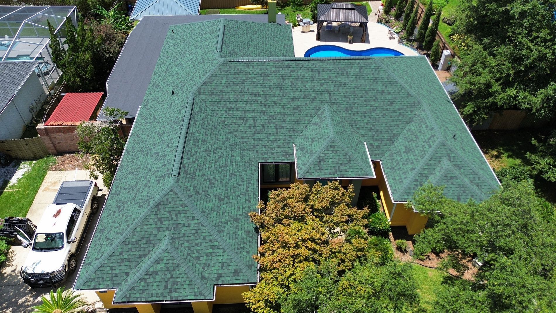 Aerial view of a large house with a green roof surrounded by trees and parked cars