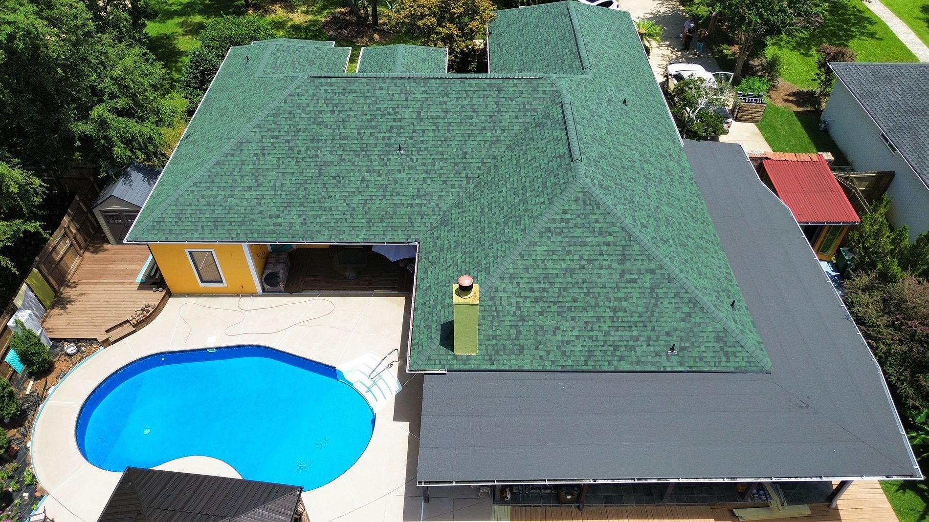 Aerial view of a house with a green roof and a bright blue backyard pool.