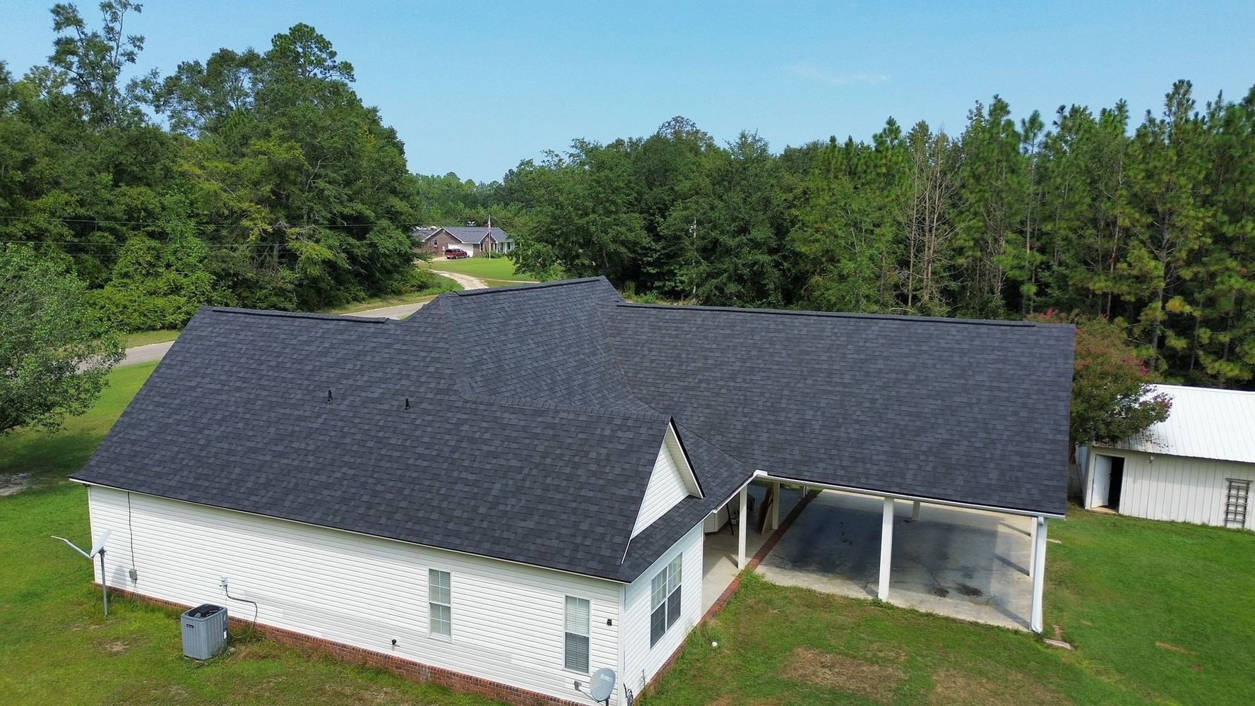 Aerial view of a white house with a dark roof, surrounded by green trees and lawn.