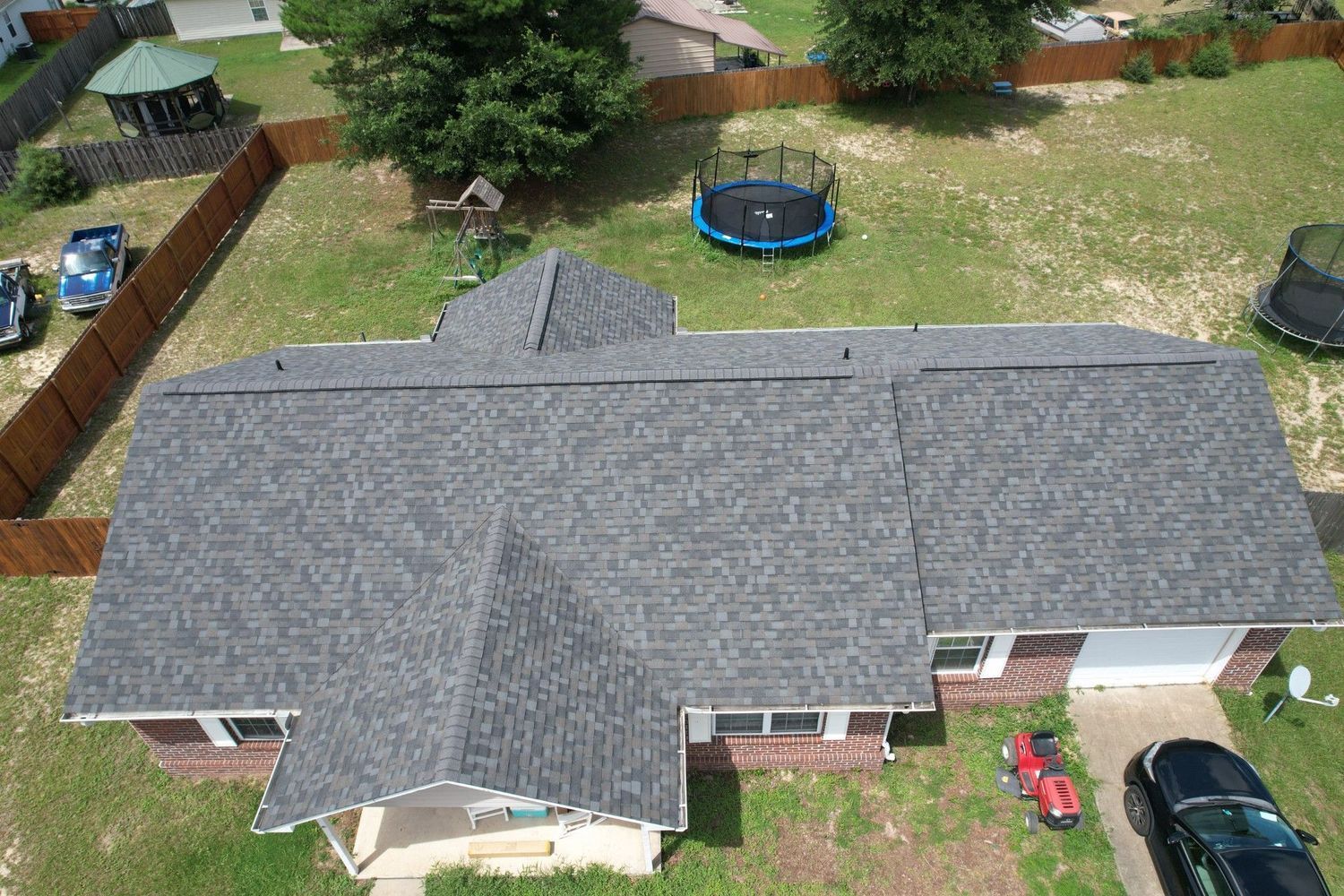 Aerial view of a house with gray roof, backyard, trampoline, and a parked car in the driveway