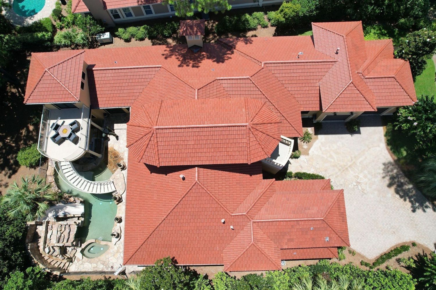 Aerial view of a large house with red tile roofs, a central courtyard, and a pool area surrounded by trees.