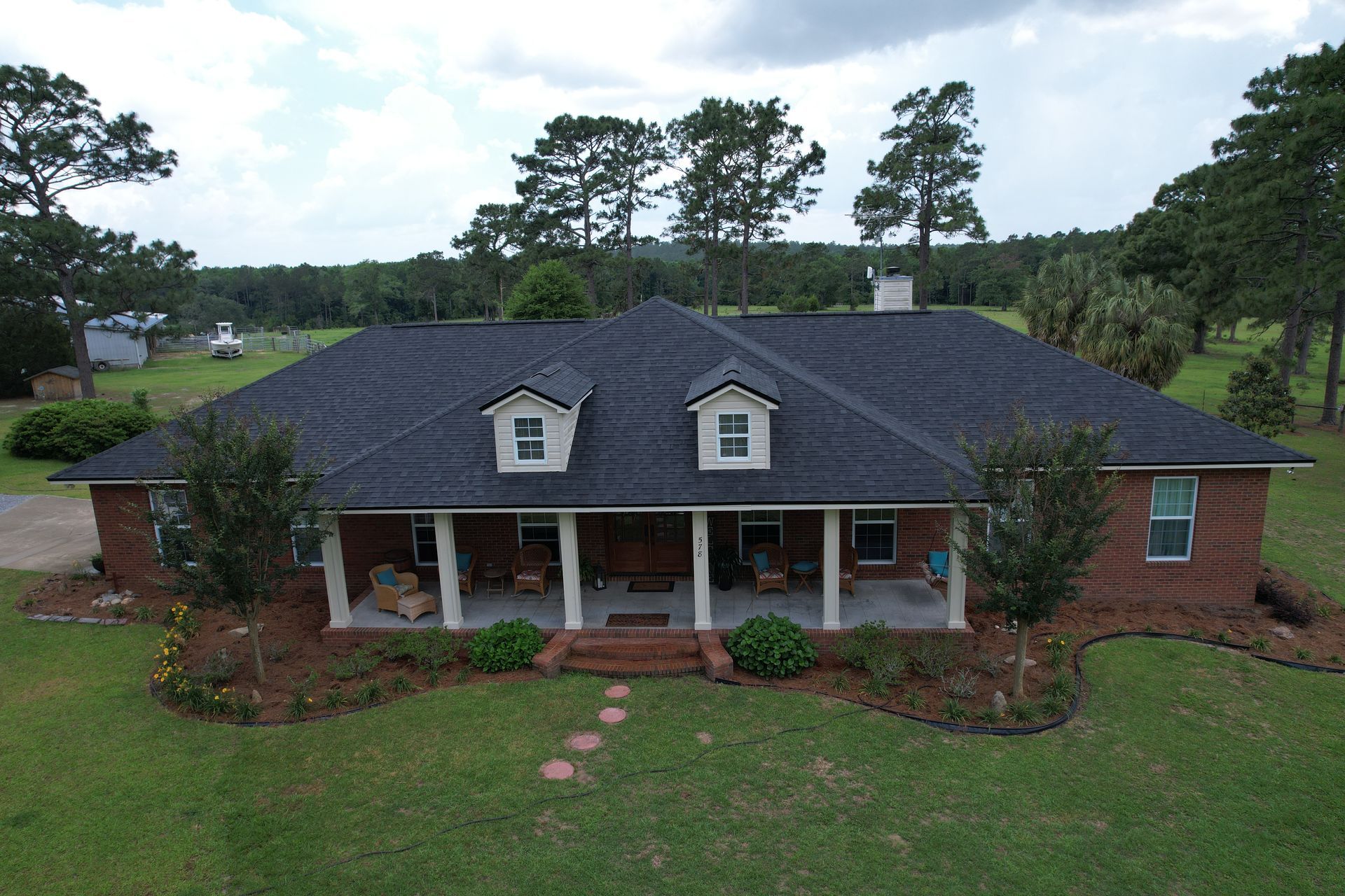 Brick house with a front porch, white columns, and a dark shingled roof in a grassy yard.