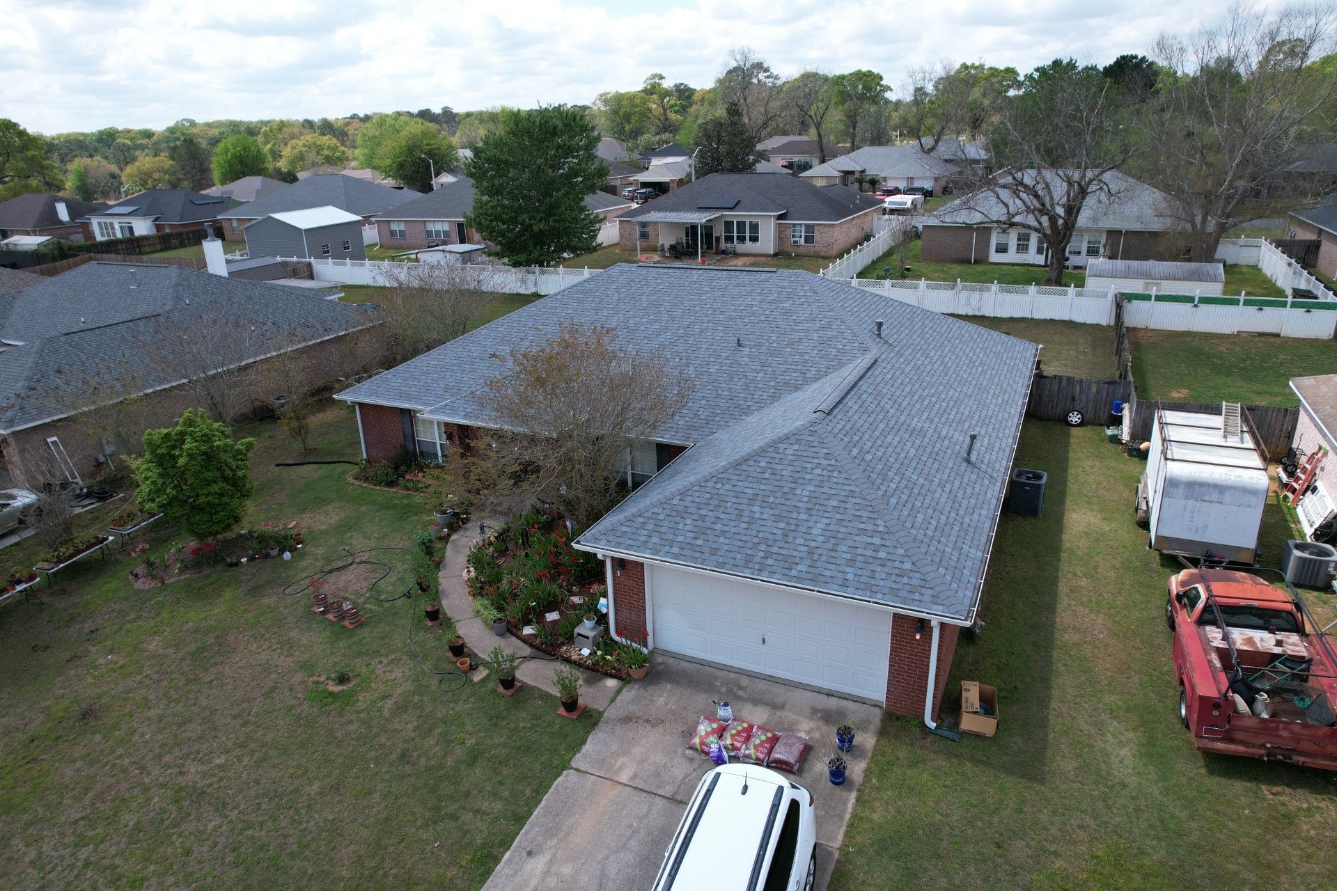 Aerial view of a suburban house with a gray roof, driveway, and parked vehicles in the yard.