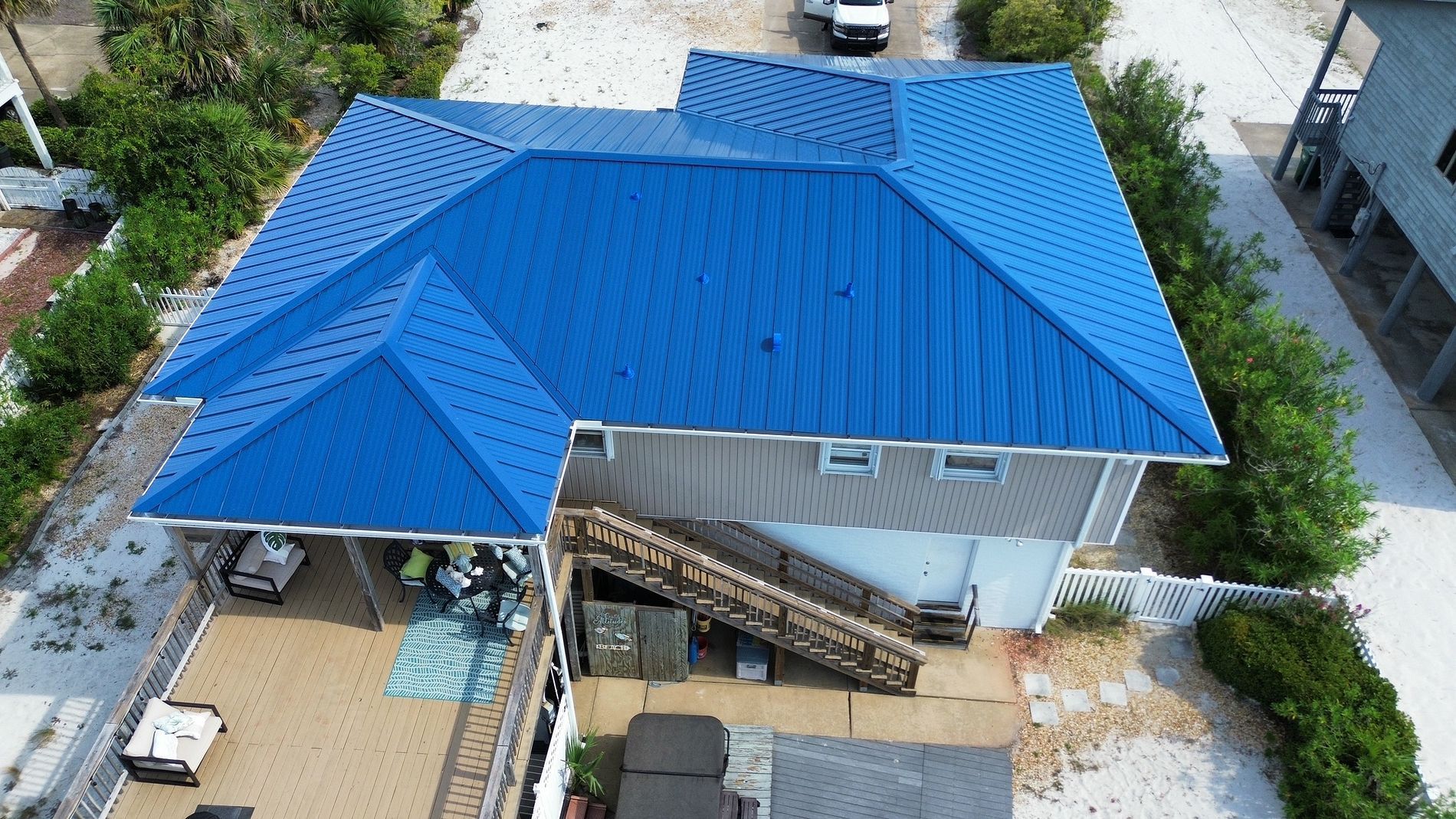 Aerial view of a house with a bright blue metal roof and surrounding yard.