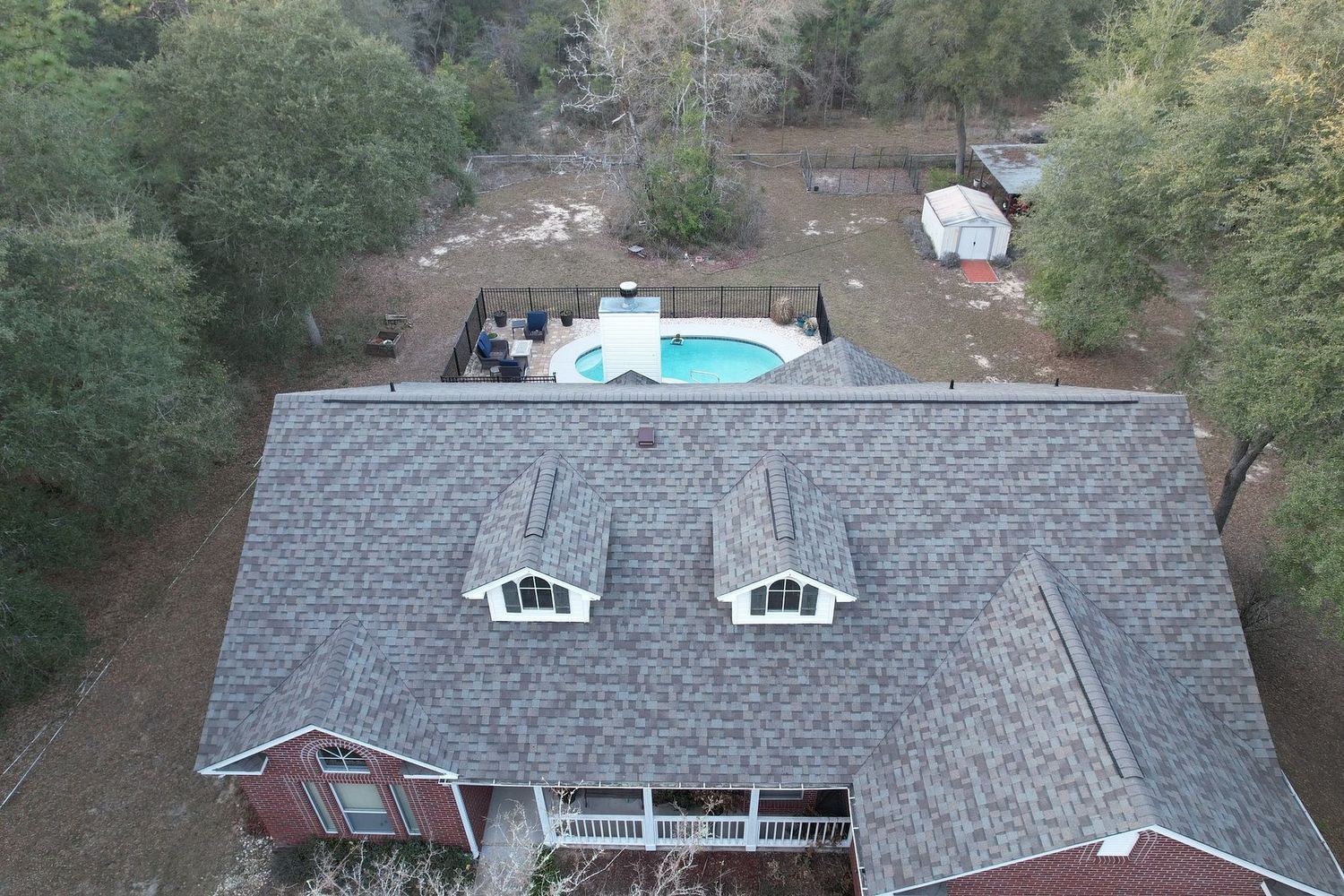 Aerial view of a house with a backyard pool, trees, and a small shed.