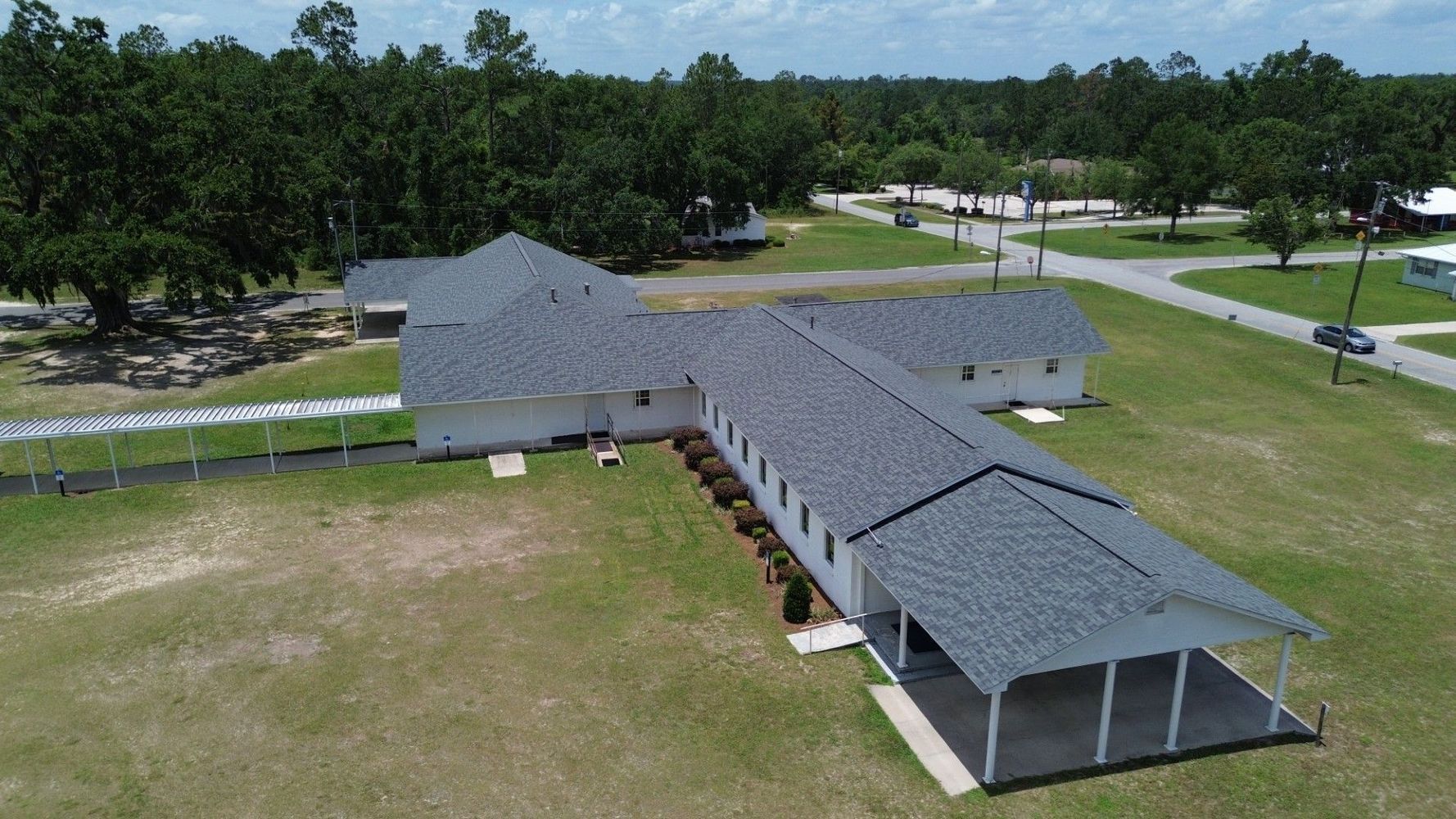 Aerial view of a gray-roofed pavilion complex on a grassy field with trees and a road nearby