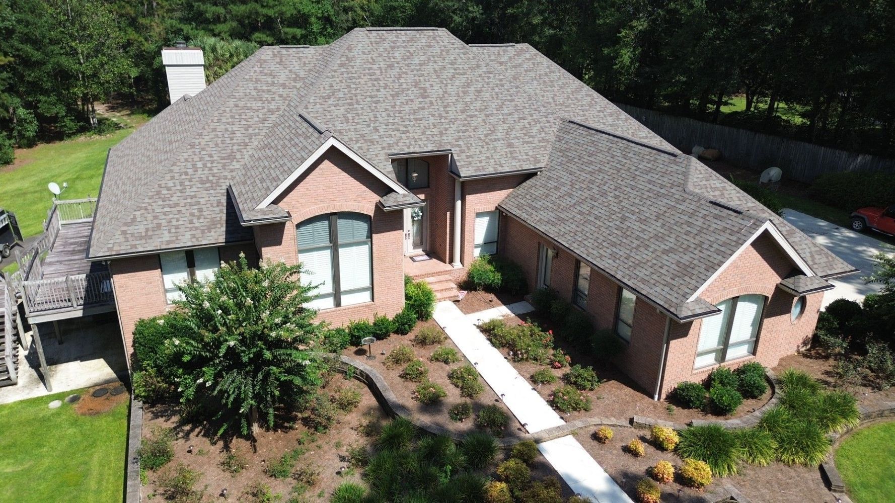 Aerial view of a brick house with a gray roof, front walkway, and landscaped yard.