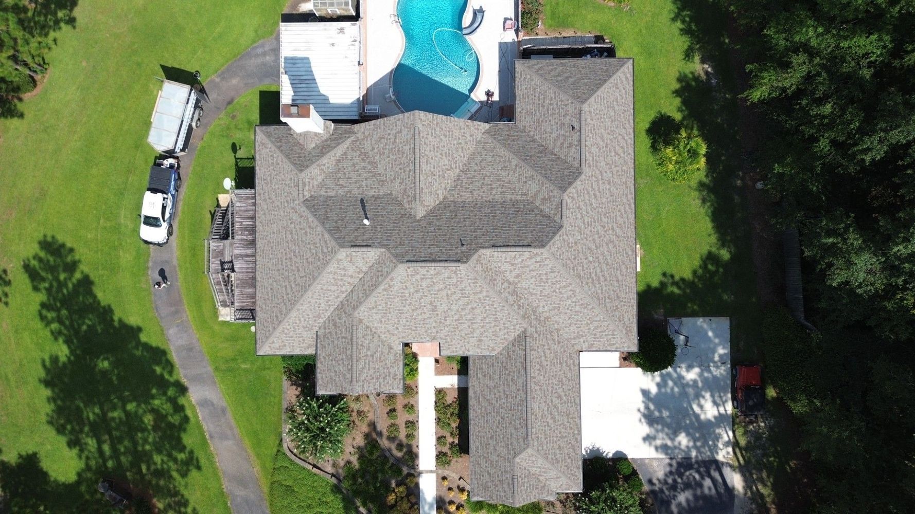 Aerial view of a suburban house with a gray roof, swimming pool, driveway, and green yard