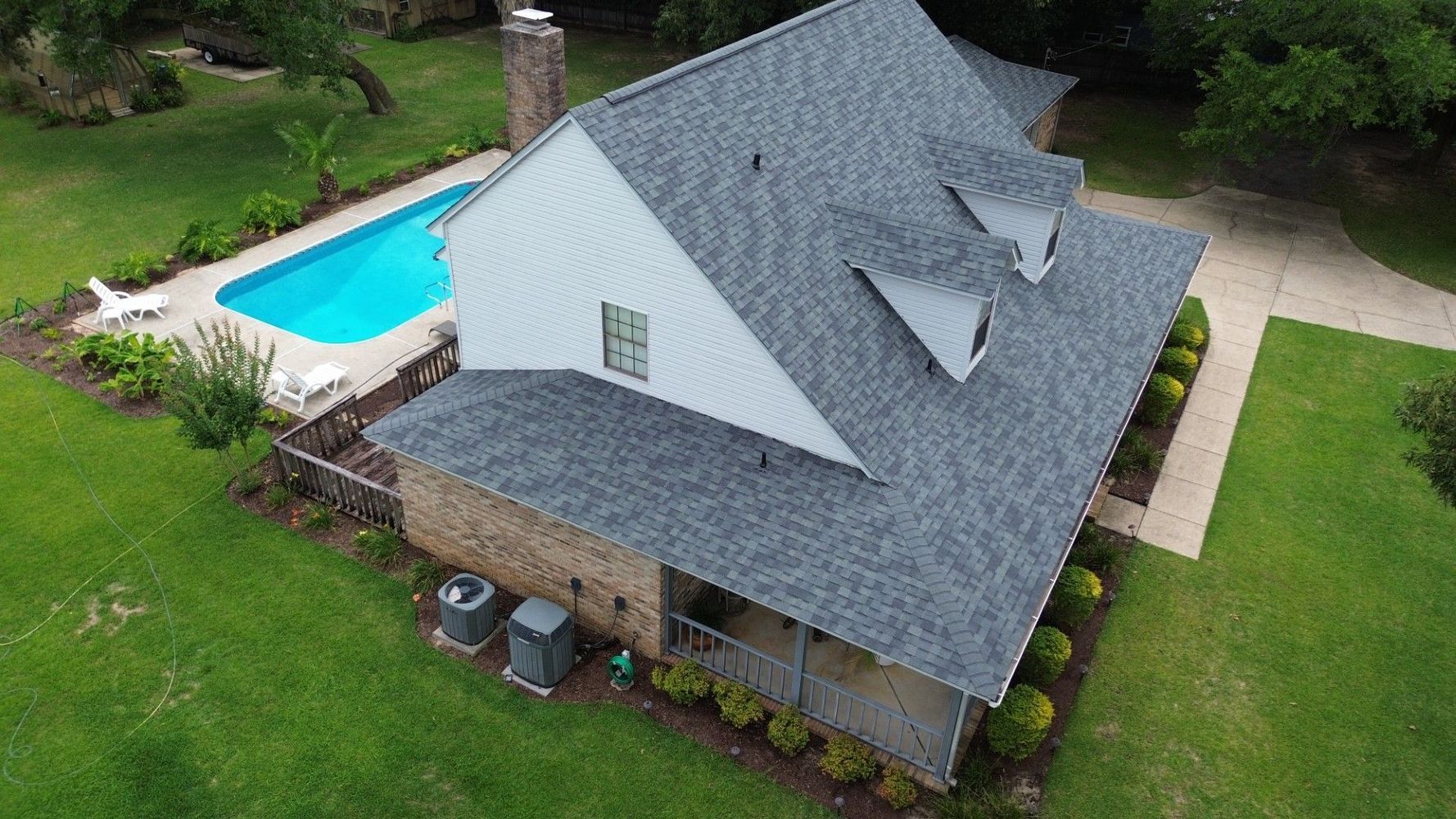 Aerial view of a house with a gray roof beside a backyard pool and green lawn.