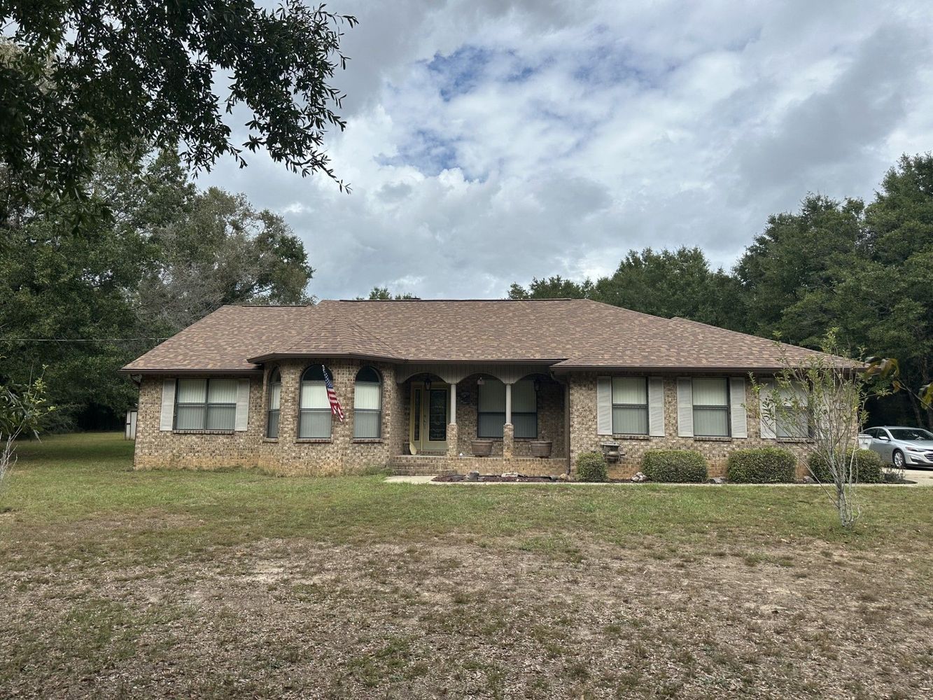 Single-story brick house with a front porch and shingled roof under a cloudy sky