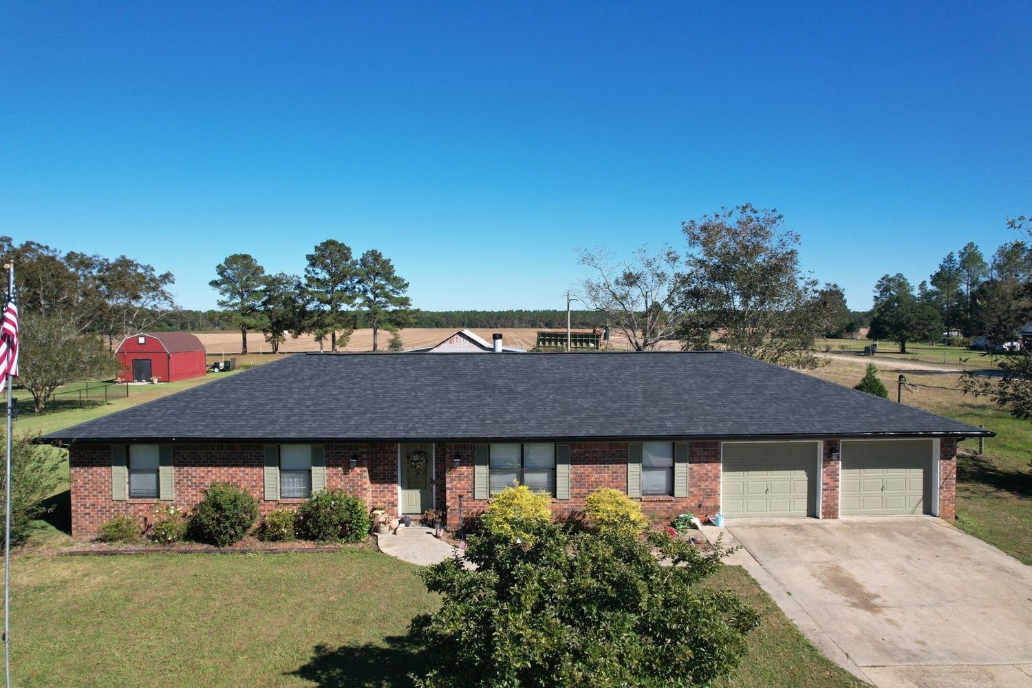 Single-story brick house with dark roof, front lawn, and attached garage under a clear blue sky