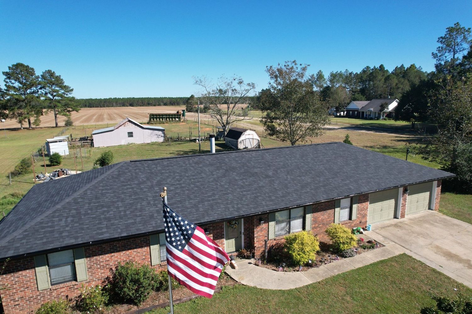 Single-story brick house with an American flag, viewed from above on a sunny rural property.