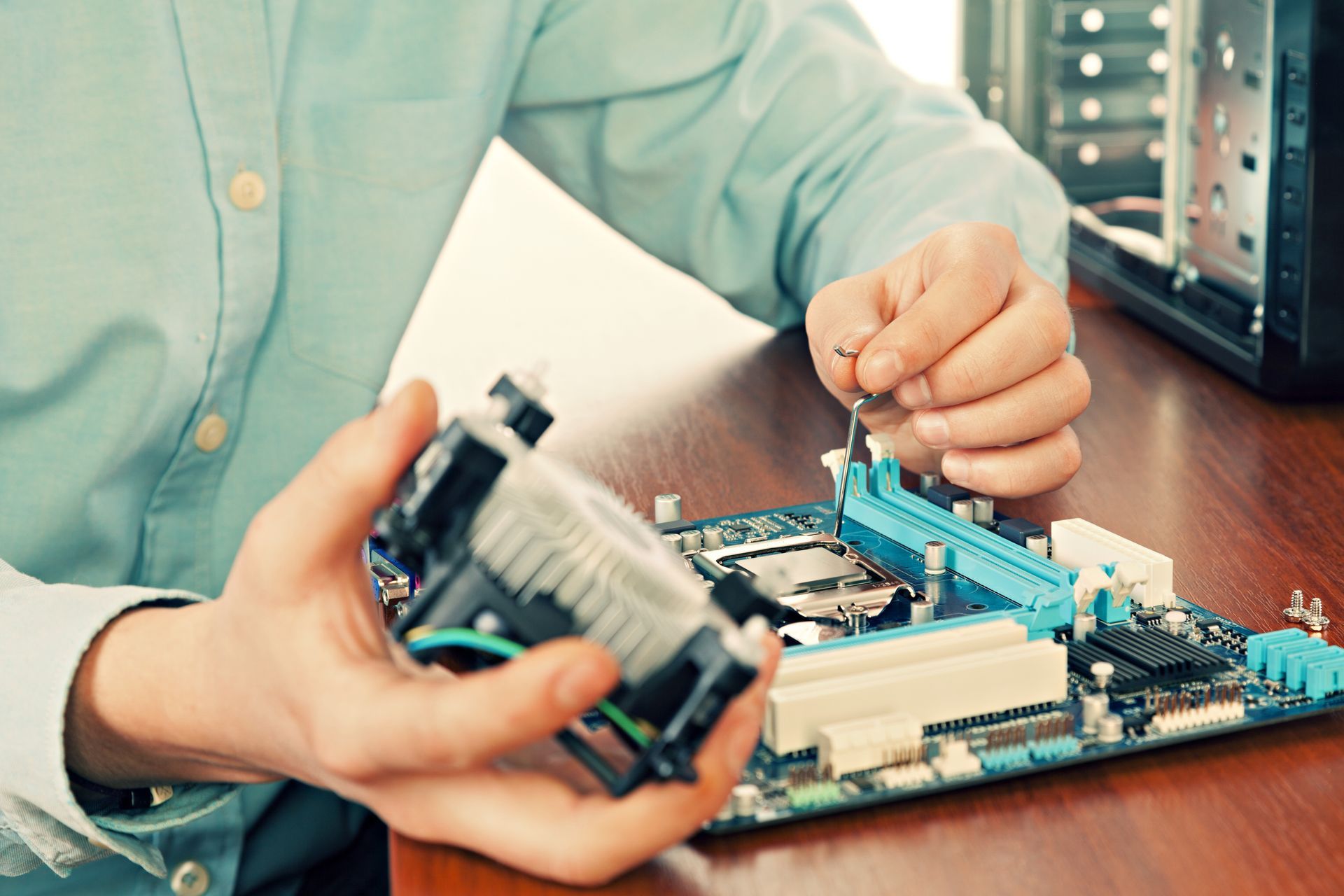 Person installing a computer component on a motherboard at a desk