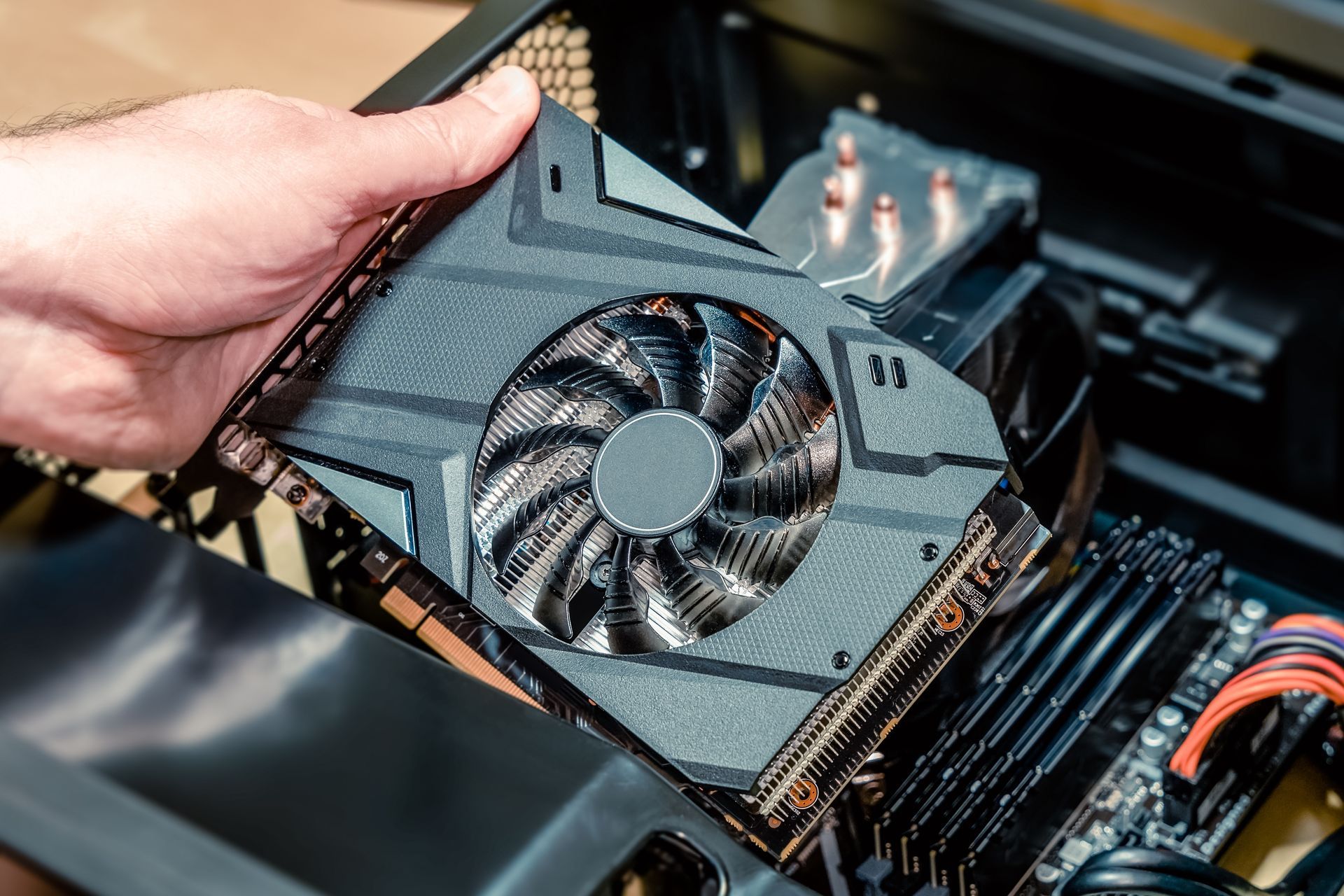 Hand holding a graphics card above an open computer case with RAM and internal components visible