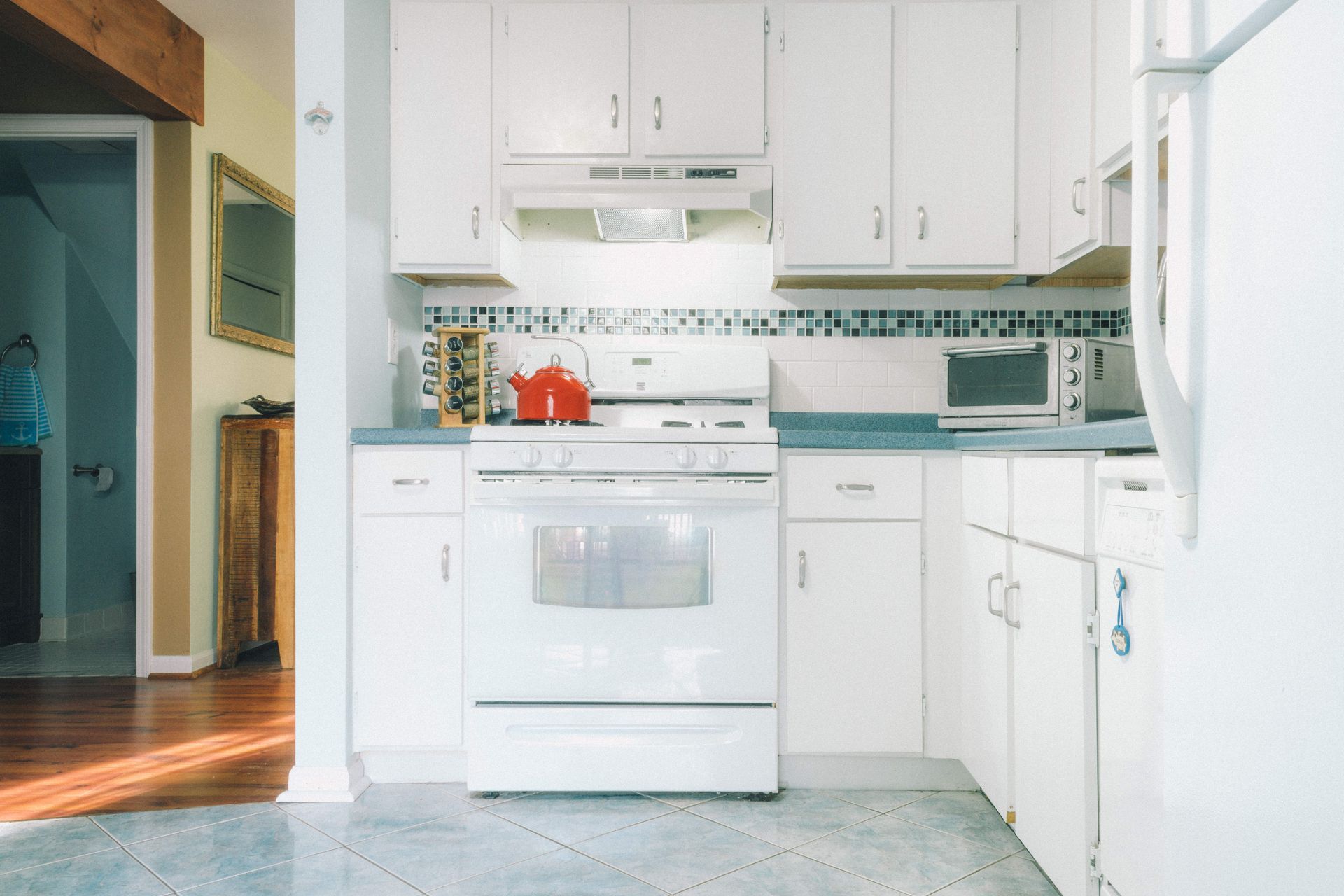 White kitchen with stove, cabinets, and appliances. A red kettle sits on the stove.