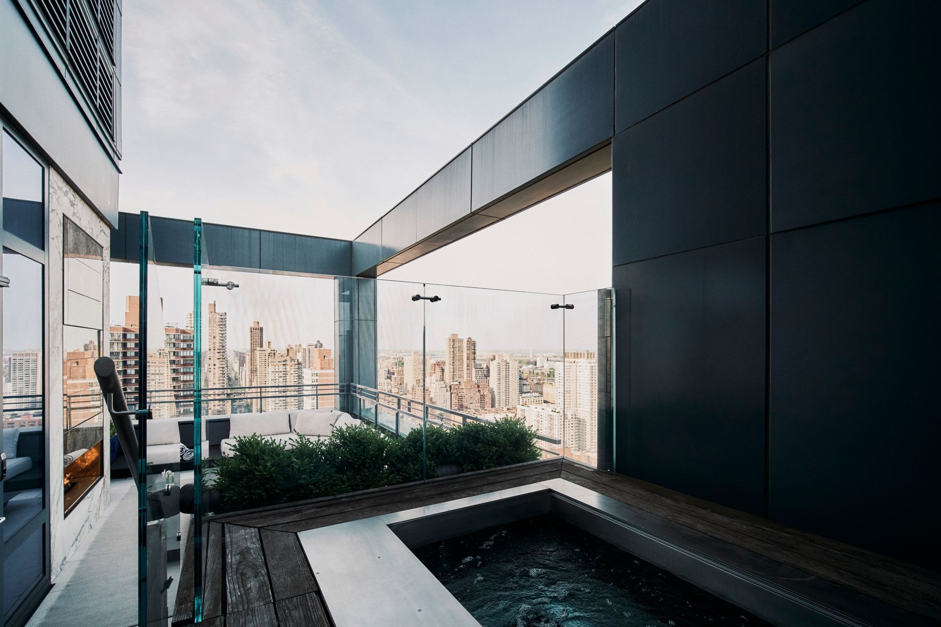Rooftop jacuzzi overlooking a city. Modern, gray building with glass barriers.