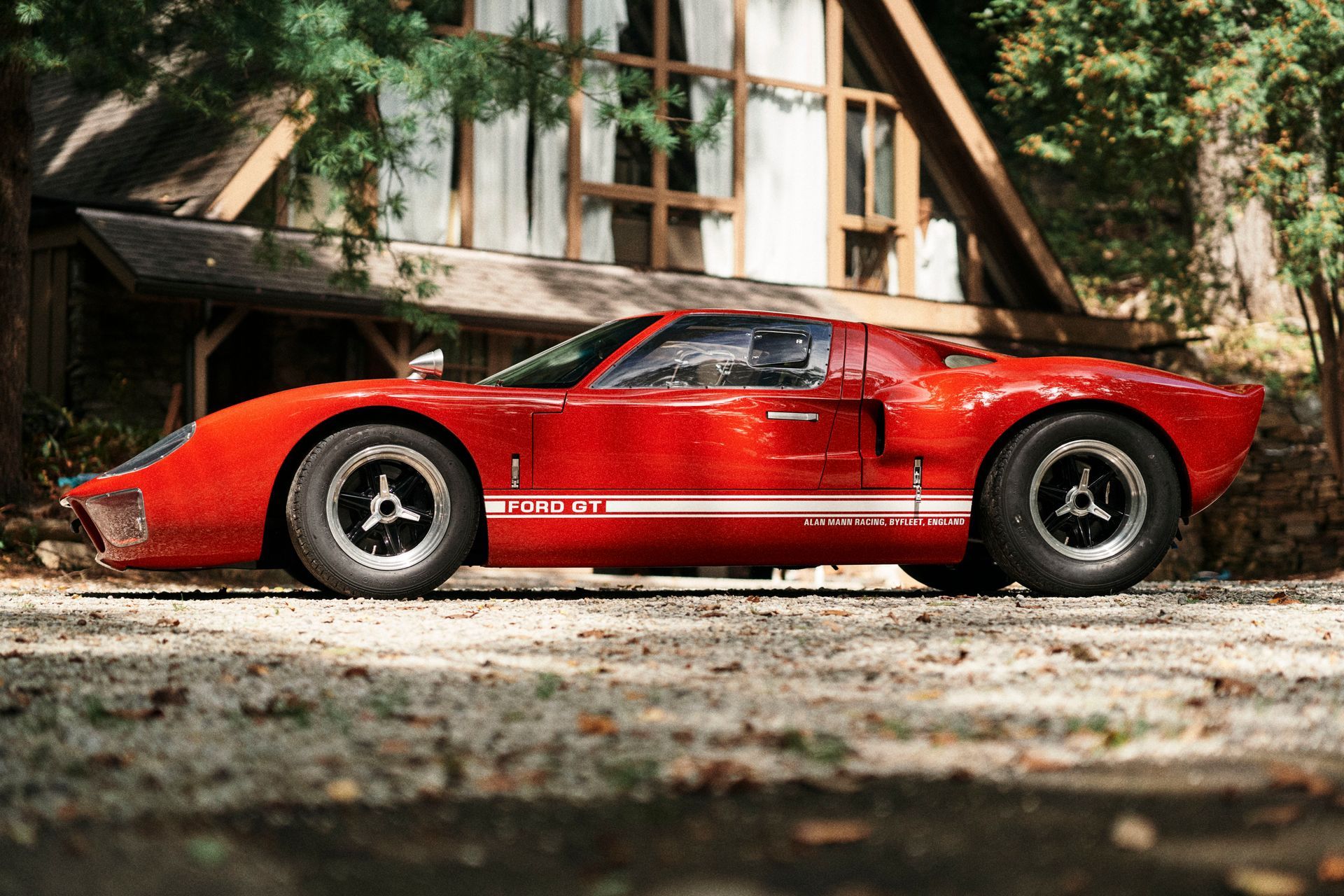 A red sports car is parked in front of a cabin in the woods.