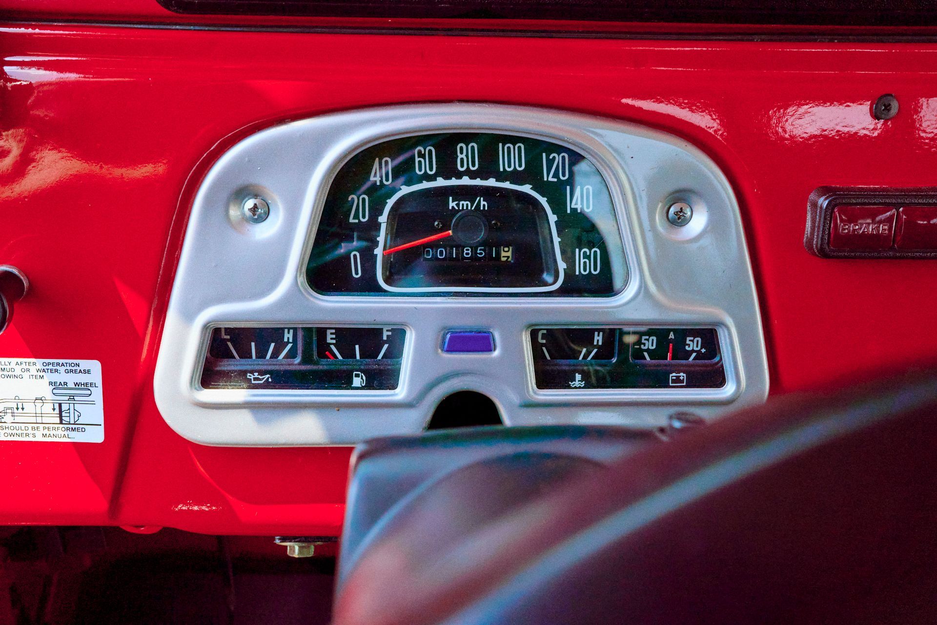 Dashboard of a red vintage car, silver instrument cluster, gauges, and a speedometer.