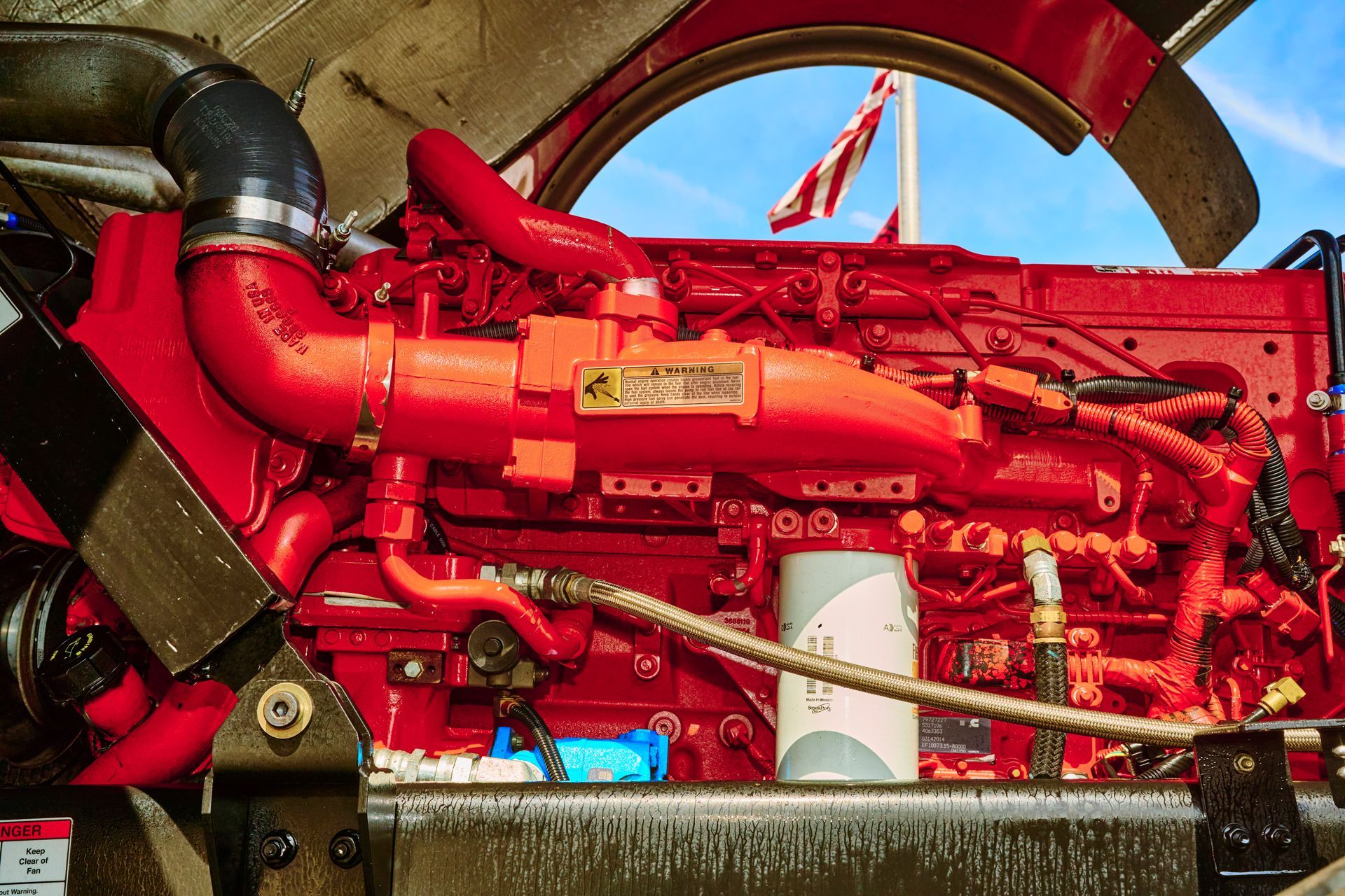 Red industrial engine with black hoses and brass fittings against a blue sky