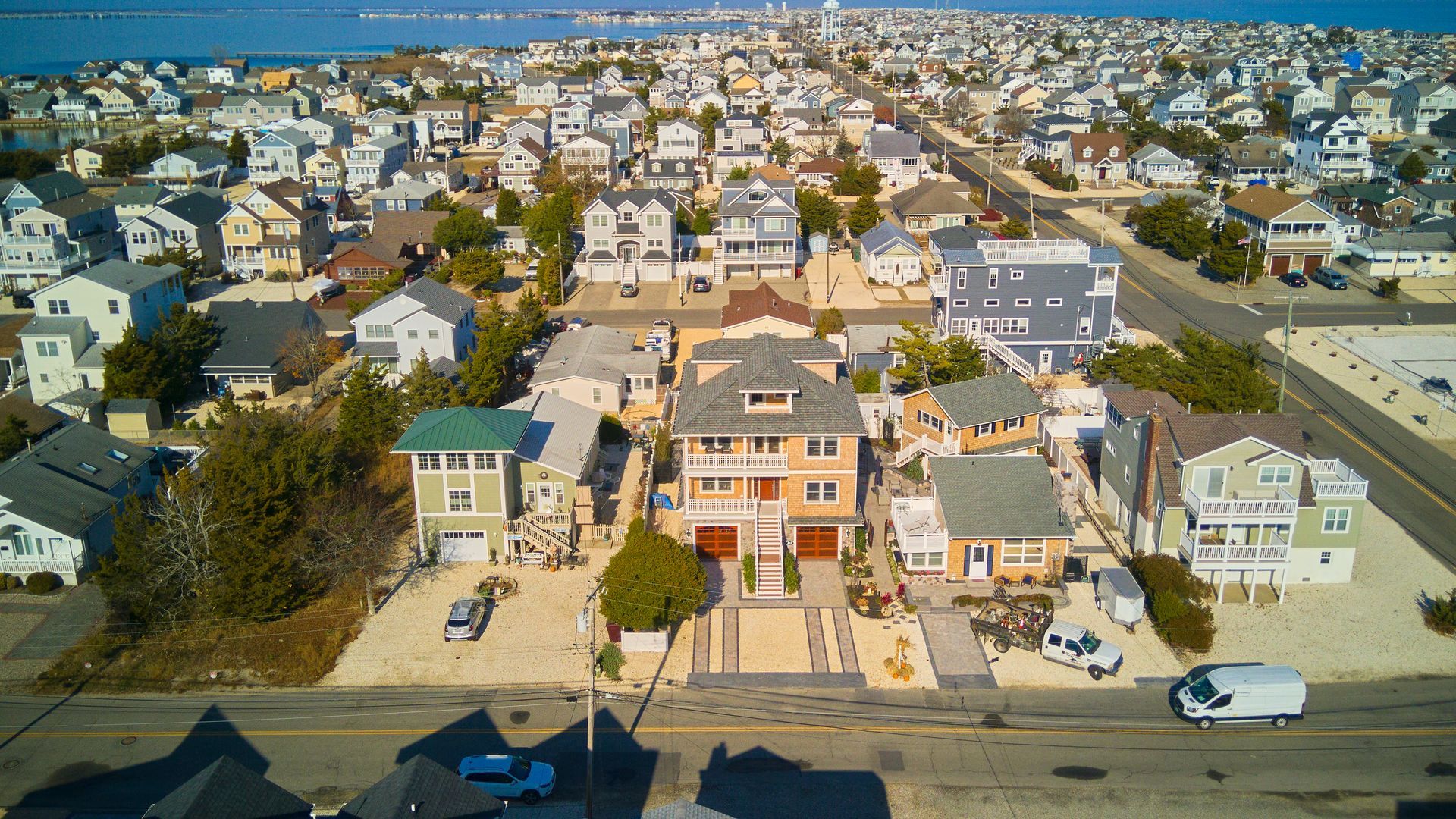 Aerial view of a coastal neighborhood with closely packed houses, mostly beige and gray, under a blue sky.