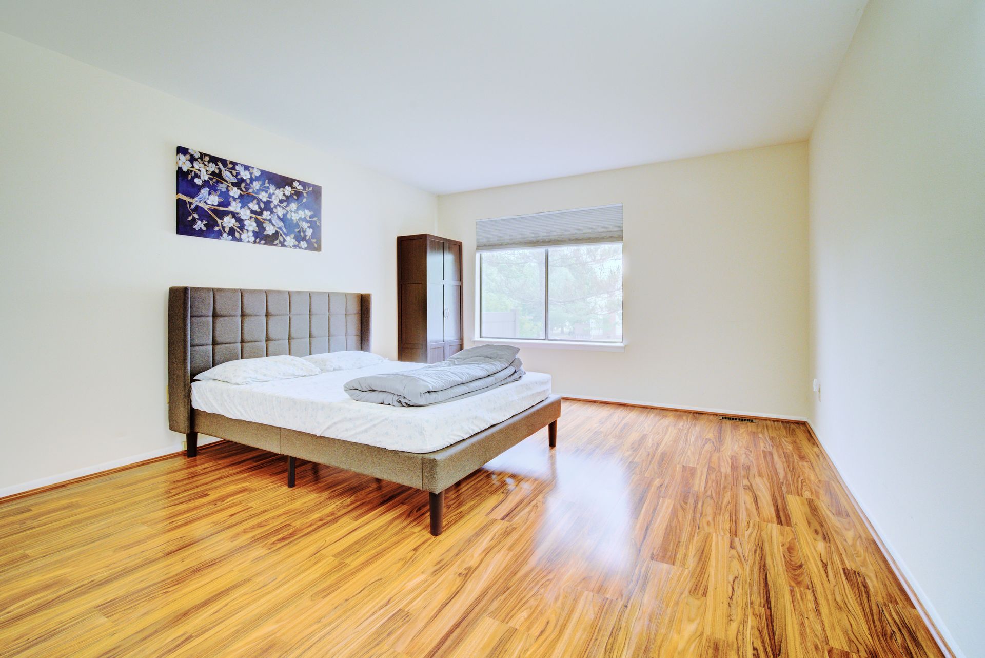 Bedroom with a bed, a wardrobe, and a window with blinds. Hardwood floor and a floral painting on the wall.