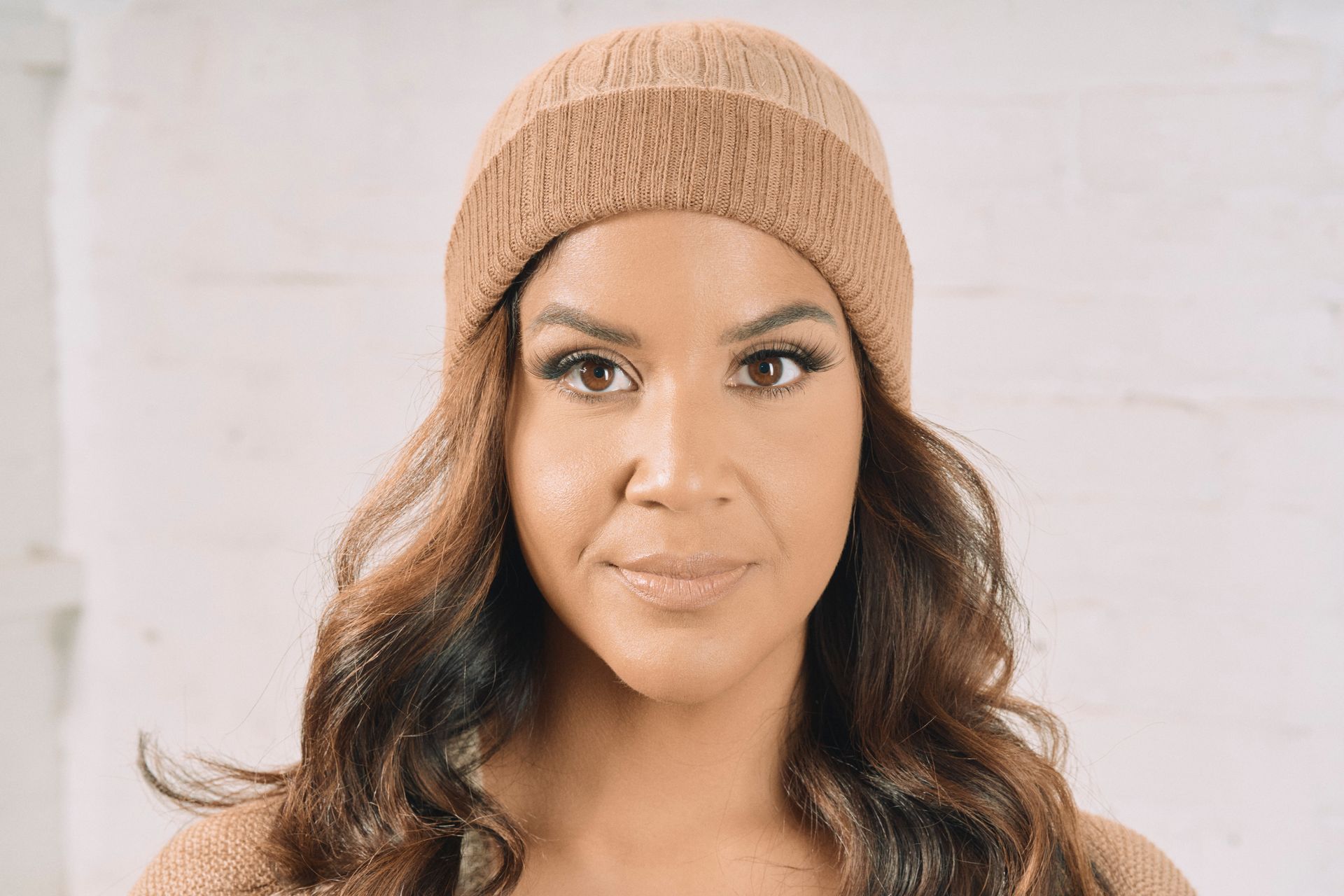 Woman wearing a light brown beanie and sweater, looking at the camera.