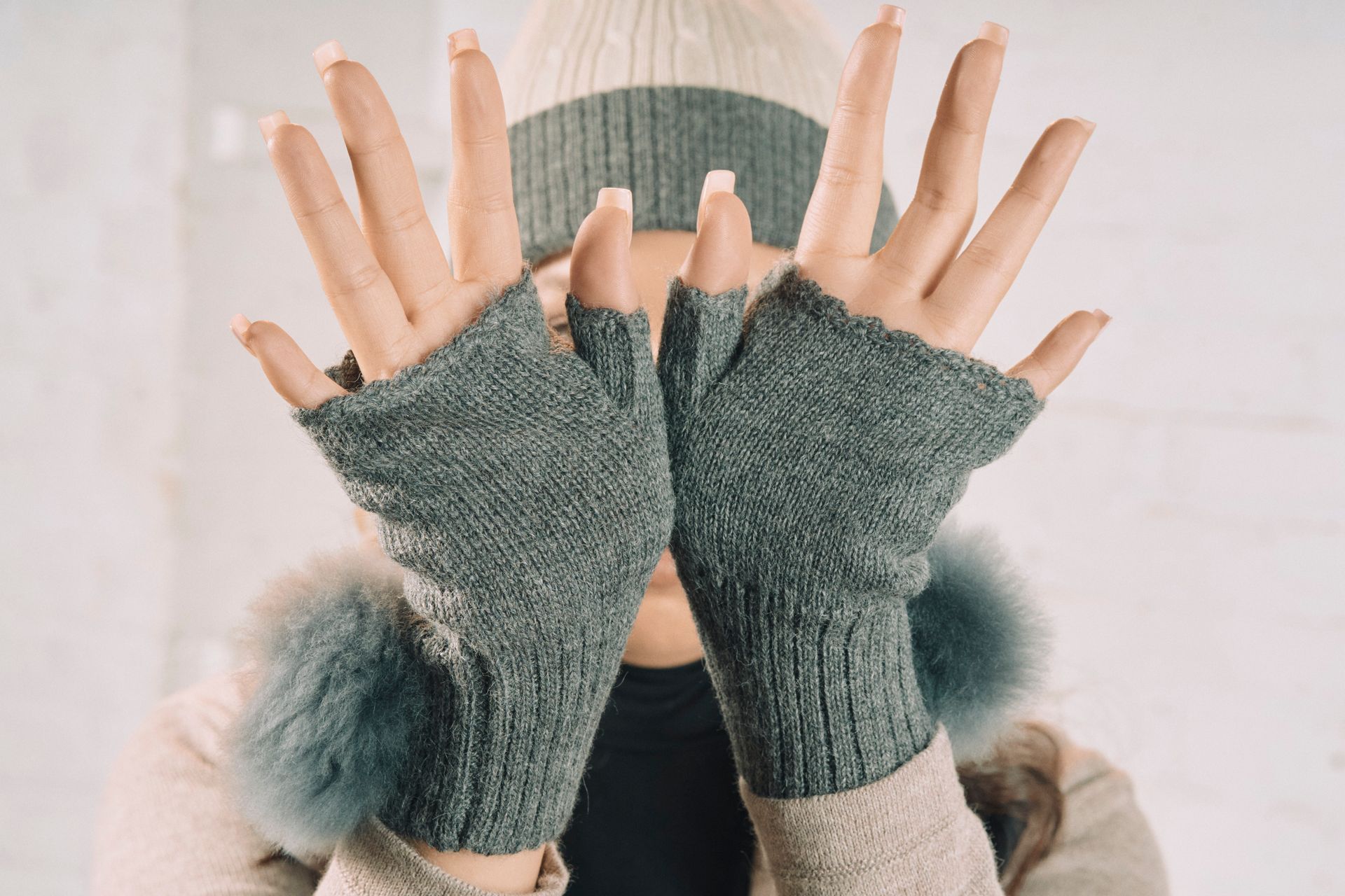 A woman wearing a hat and gloves is covering her face with her hands.