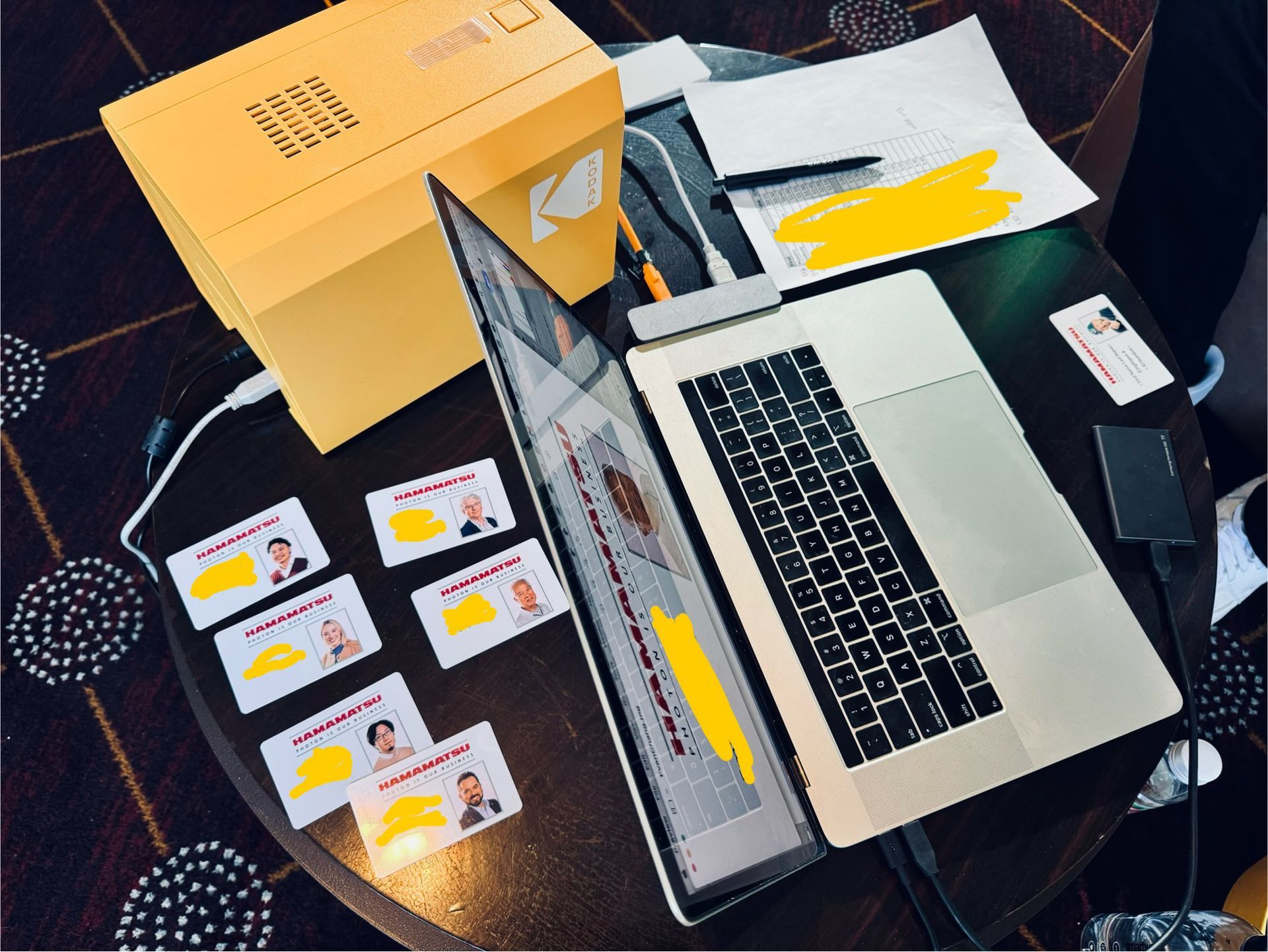 Laptop, cards, and a yellow box on a table. Cards feature photos and text. Laptop shows a document.