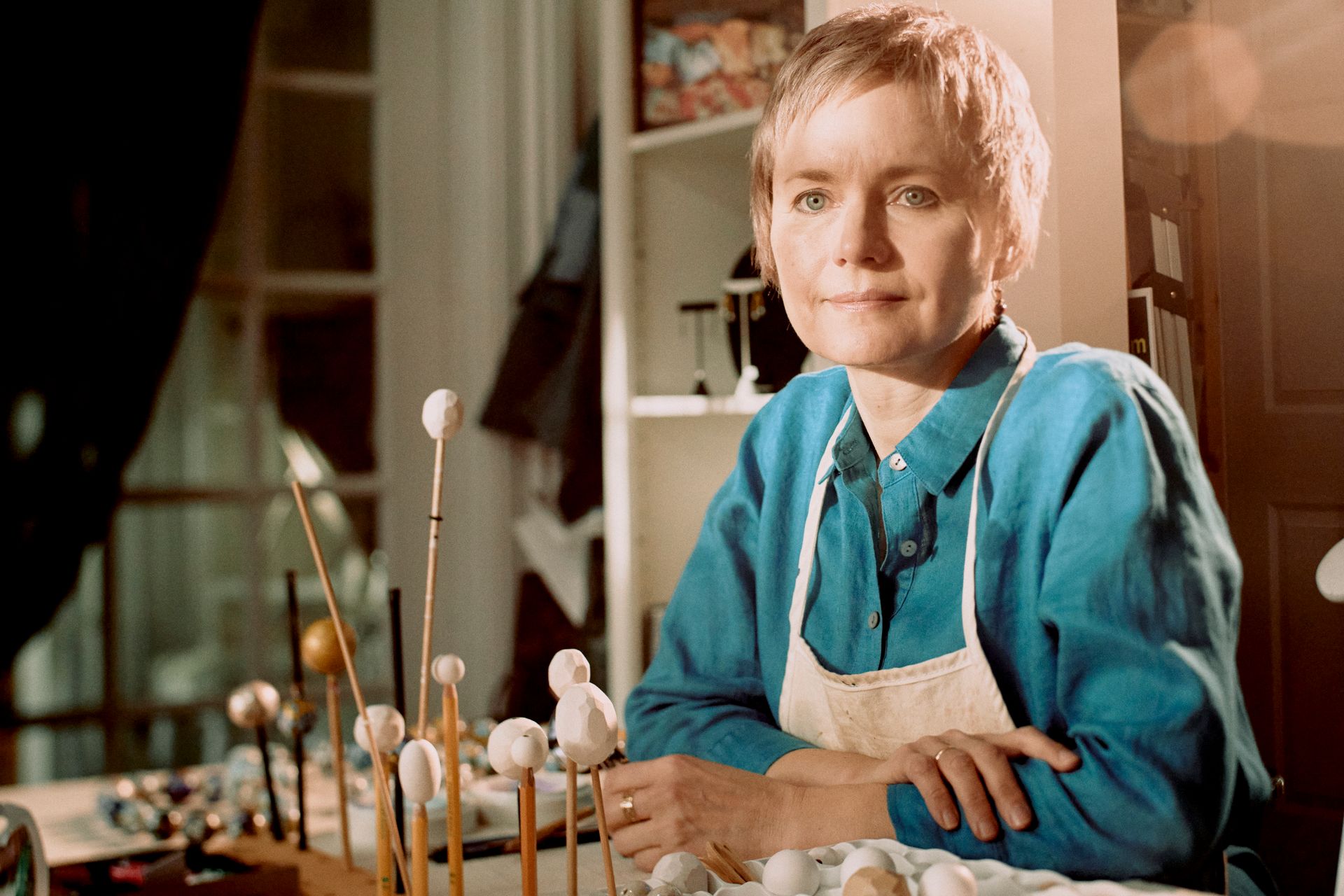 A woman in a blue shirt and apron is sitting at a table.