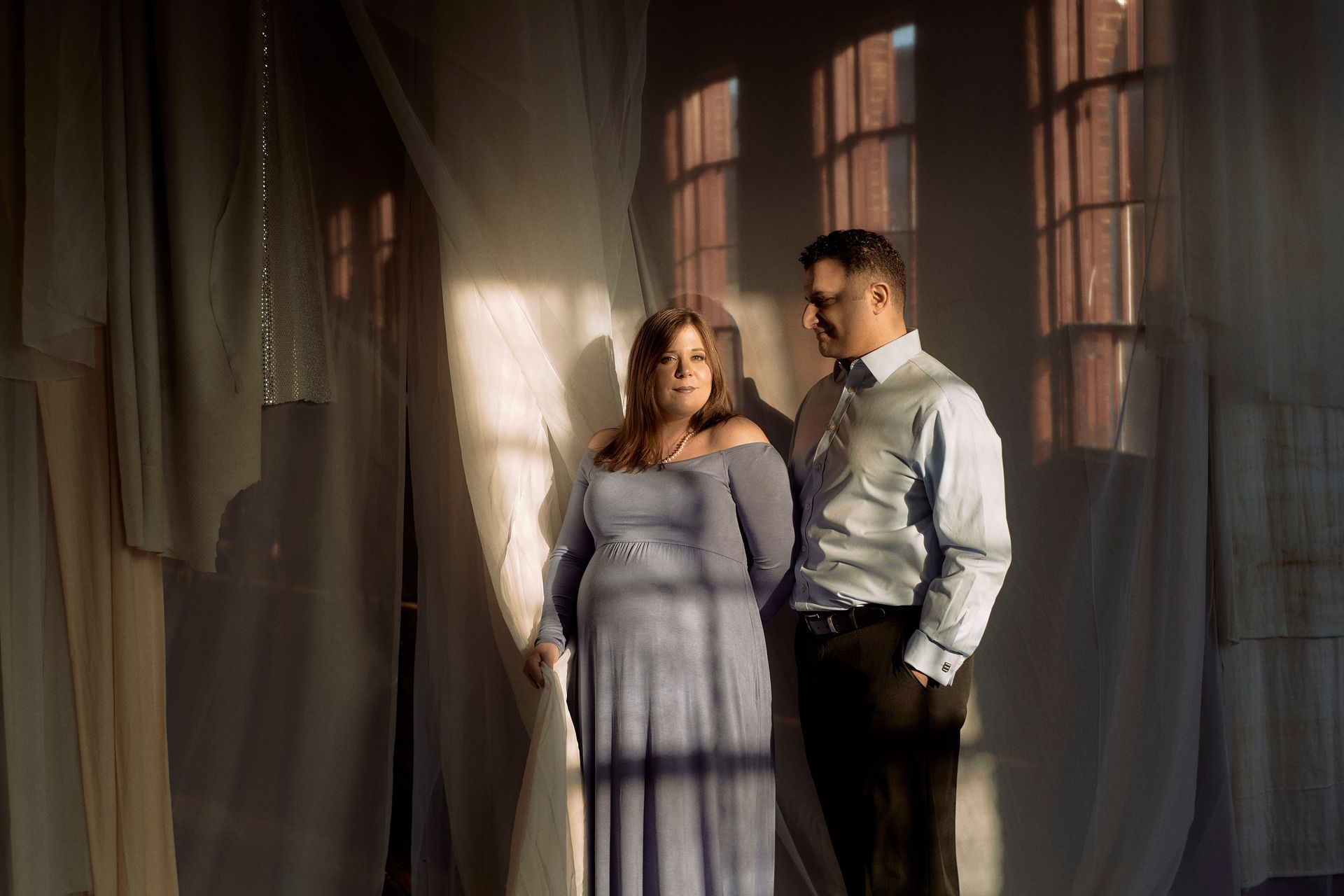 A man and a woman are standing next to each other in front of a window.