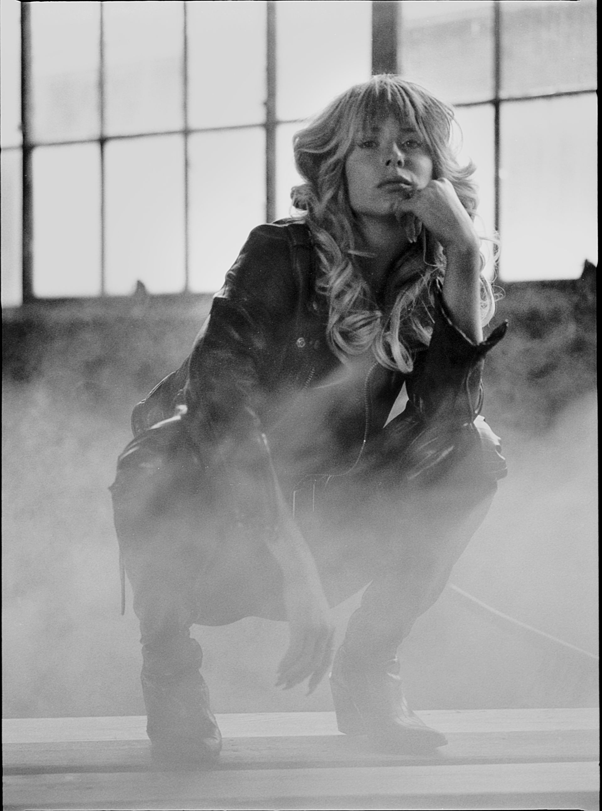 A woman is squatting down in front of a window in a black and white photo.