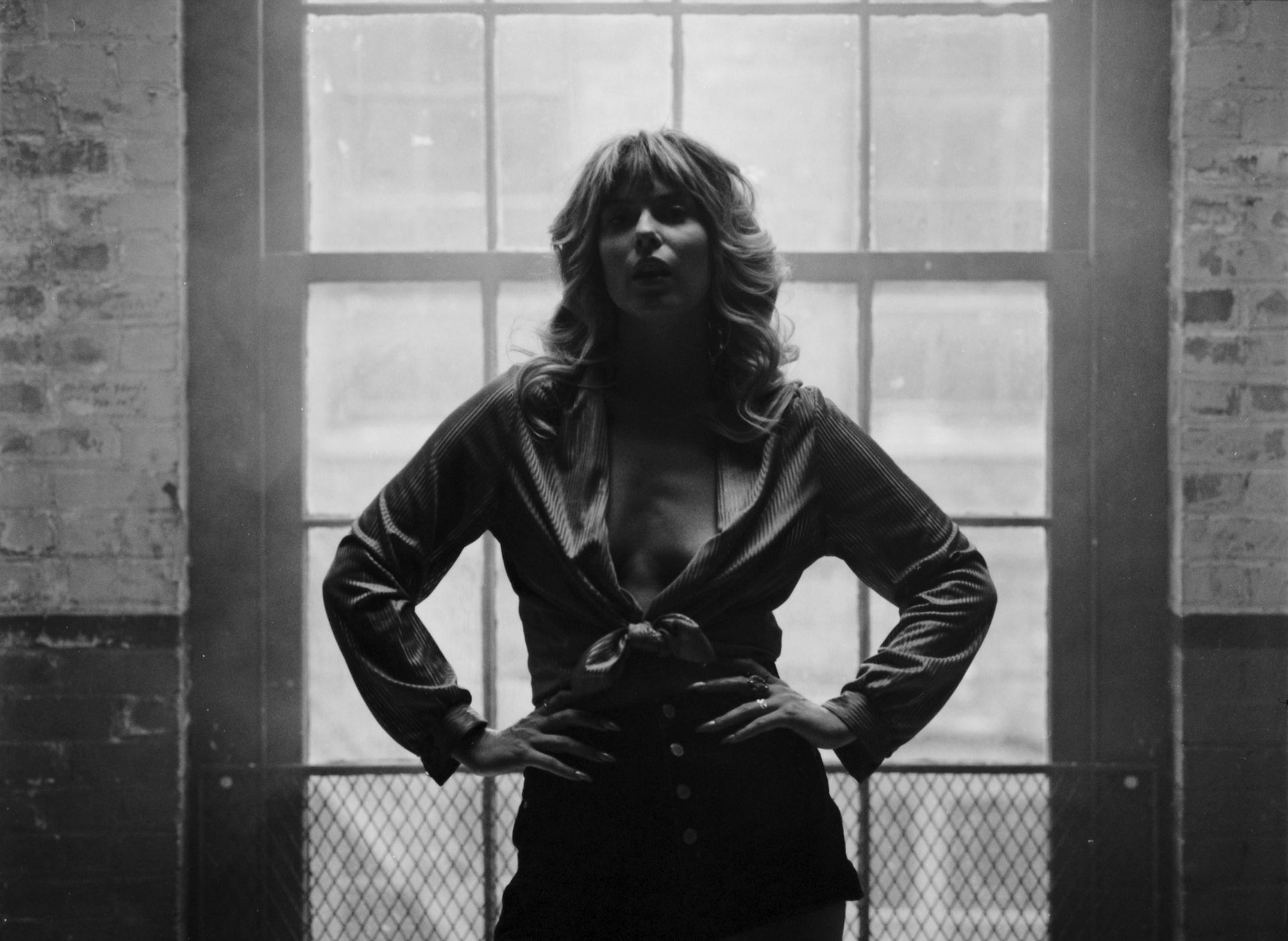 A woman is standing in front of a window with her hands on her hips.