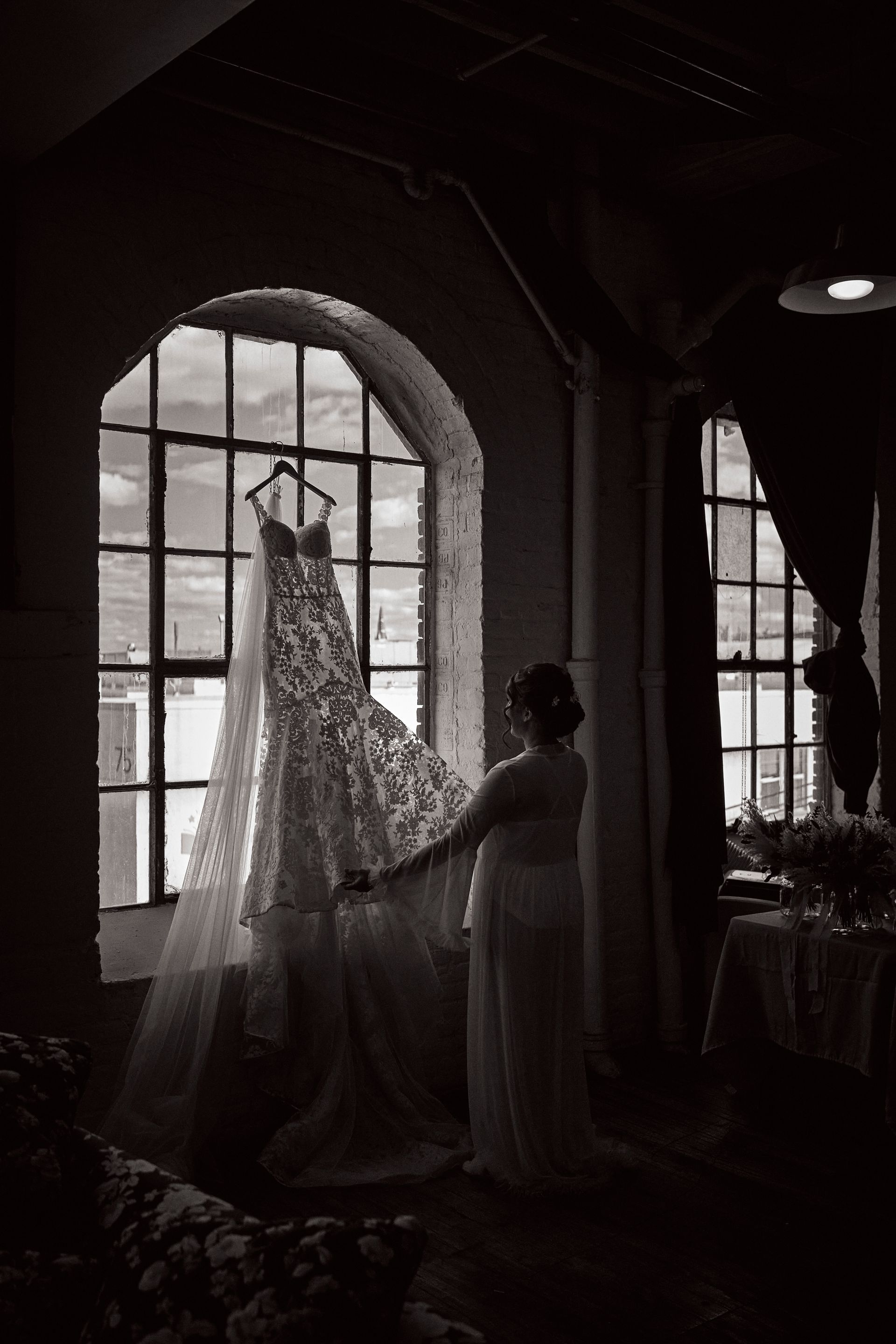 A woman is holding a wedding dress in front of a window.