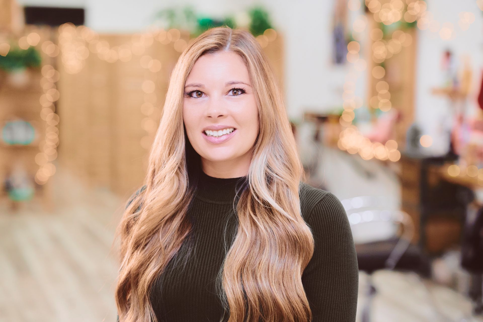 Woman with long wavy hair smiles in a salon setting.